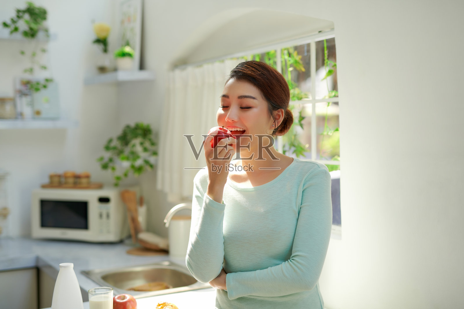 美丽的女孩拿着红苹果站在家里的厨房早上照片摄影图片