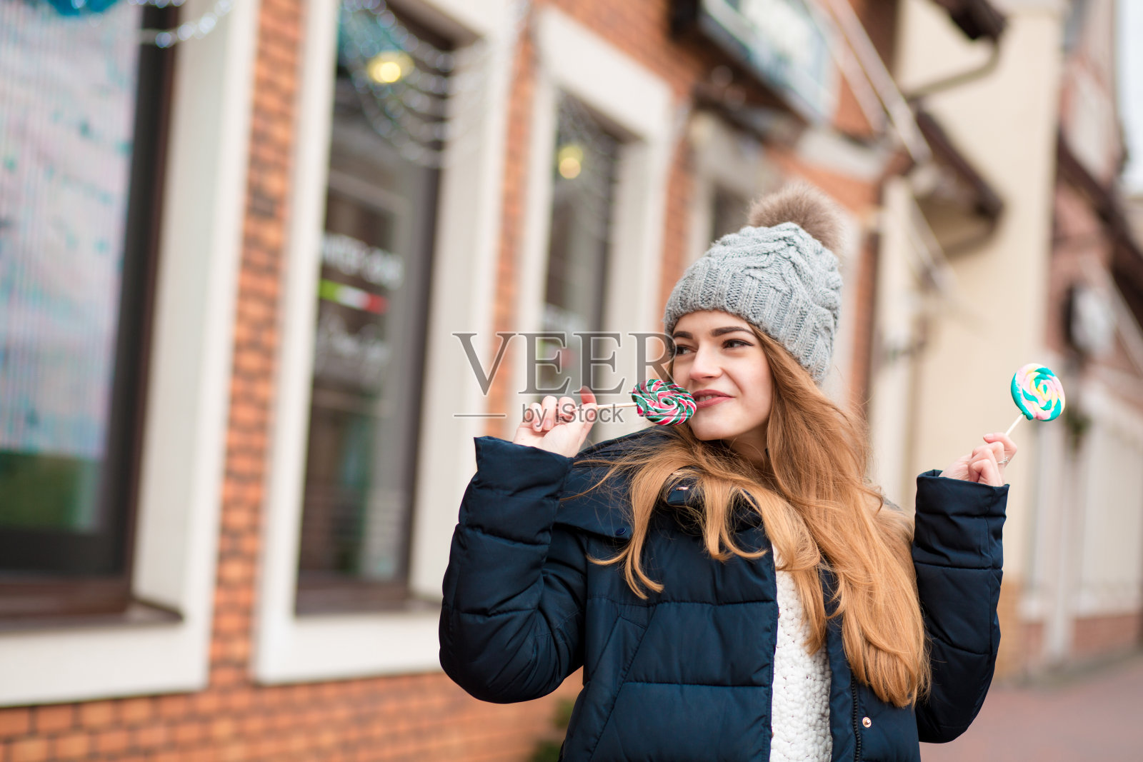 快乐的红发女人戴着灰色针织帽,吃着圣诞糖果照片摄影图片