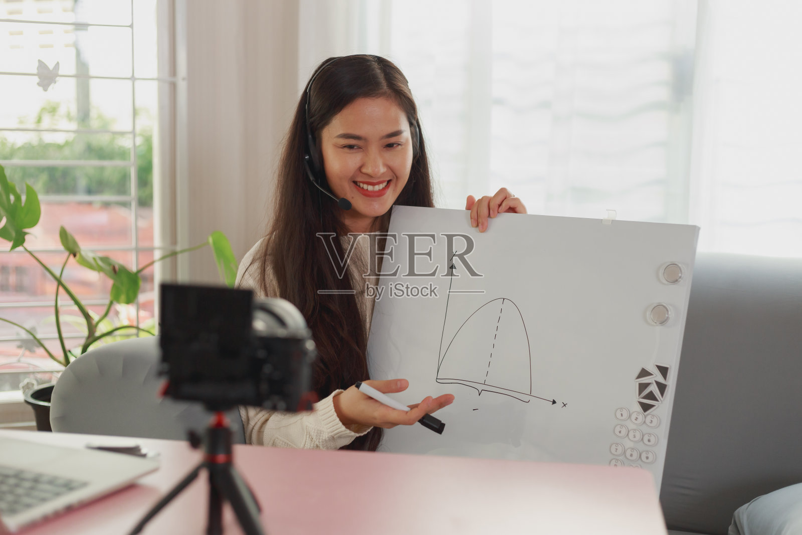 年轻的亚洲女教师的肖像工作在家庭直播教学在线视频会议。老师在白板上写字,用耳机通过互联网交流照片摄影图片