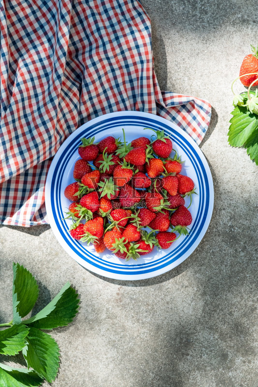 混凝土背景上的盘子上的草莓,夏天的静物。平躺,俯视图。照片摄影图片