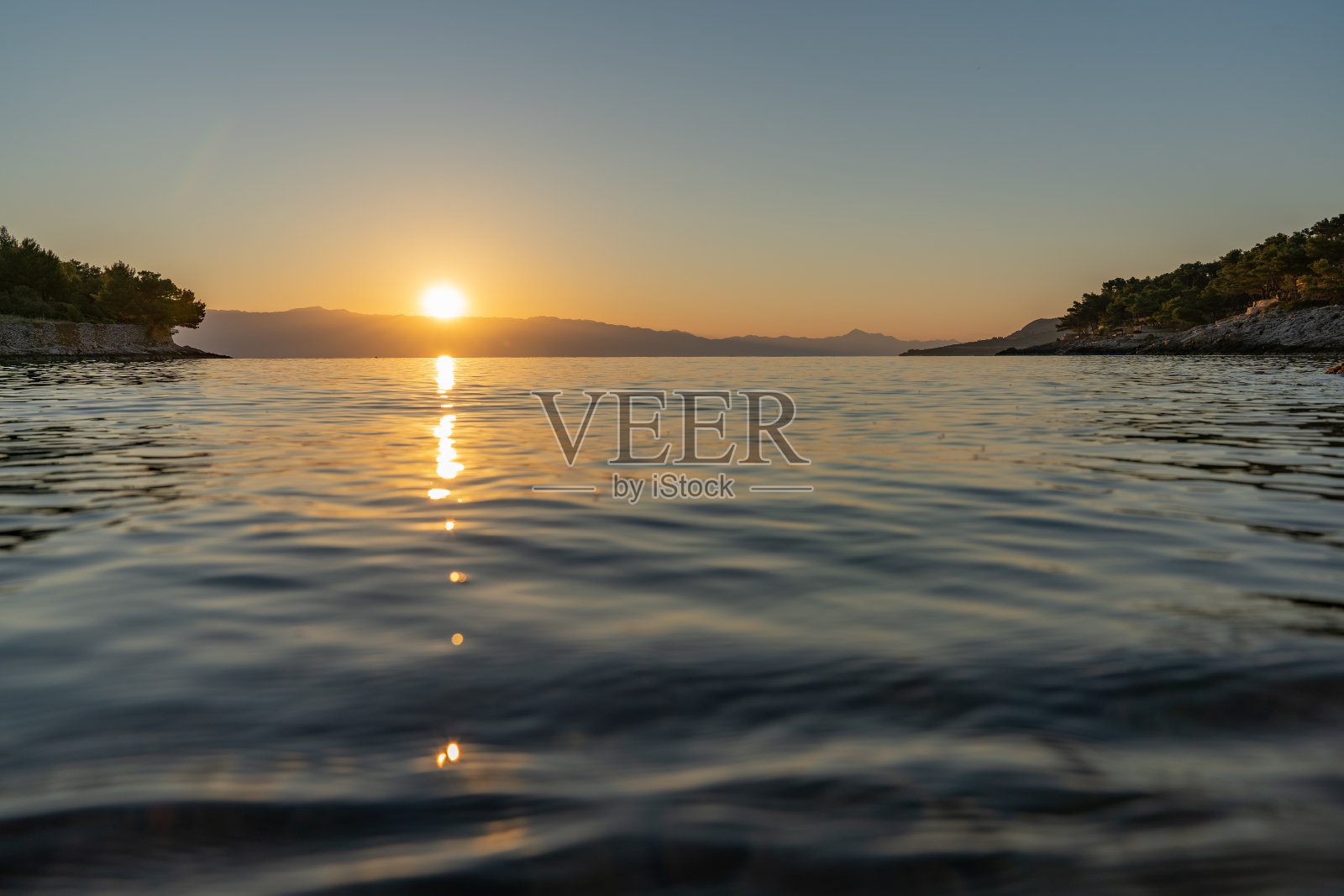 太阳刚好在海平面上,形成了日出/日落和岩石海滩的全景照片摄影图片