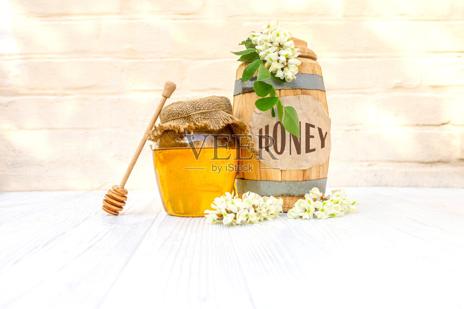 文本蜂蜜。新鲜的金合欢液体蜂蜜将于2021年在木桶和一个透明的罐子中收获,盖子上有一块帆布餐巾。花枝白色的金合欢照片摄影图片