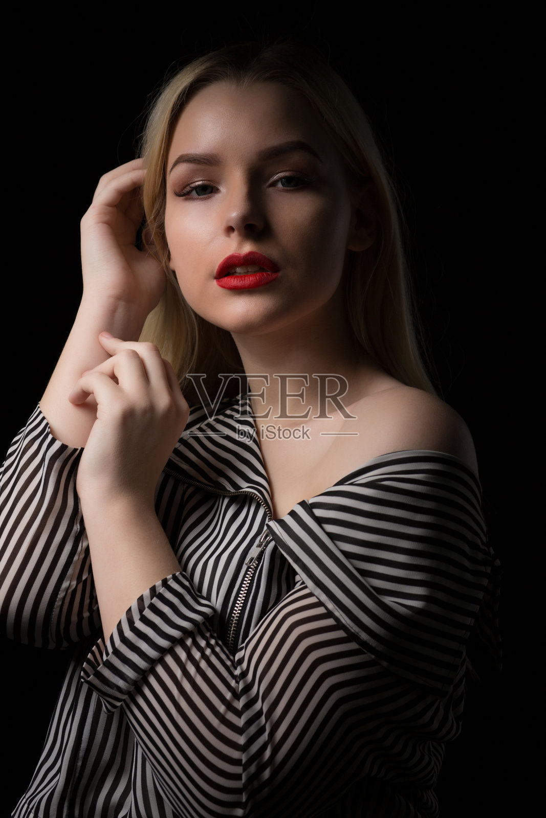 戏剧性的肖像,可爱的金发女人与红色的嘴唇穿着条纹衬衫,在黑暗中摆姿势照片摄影图片