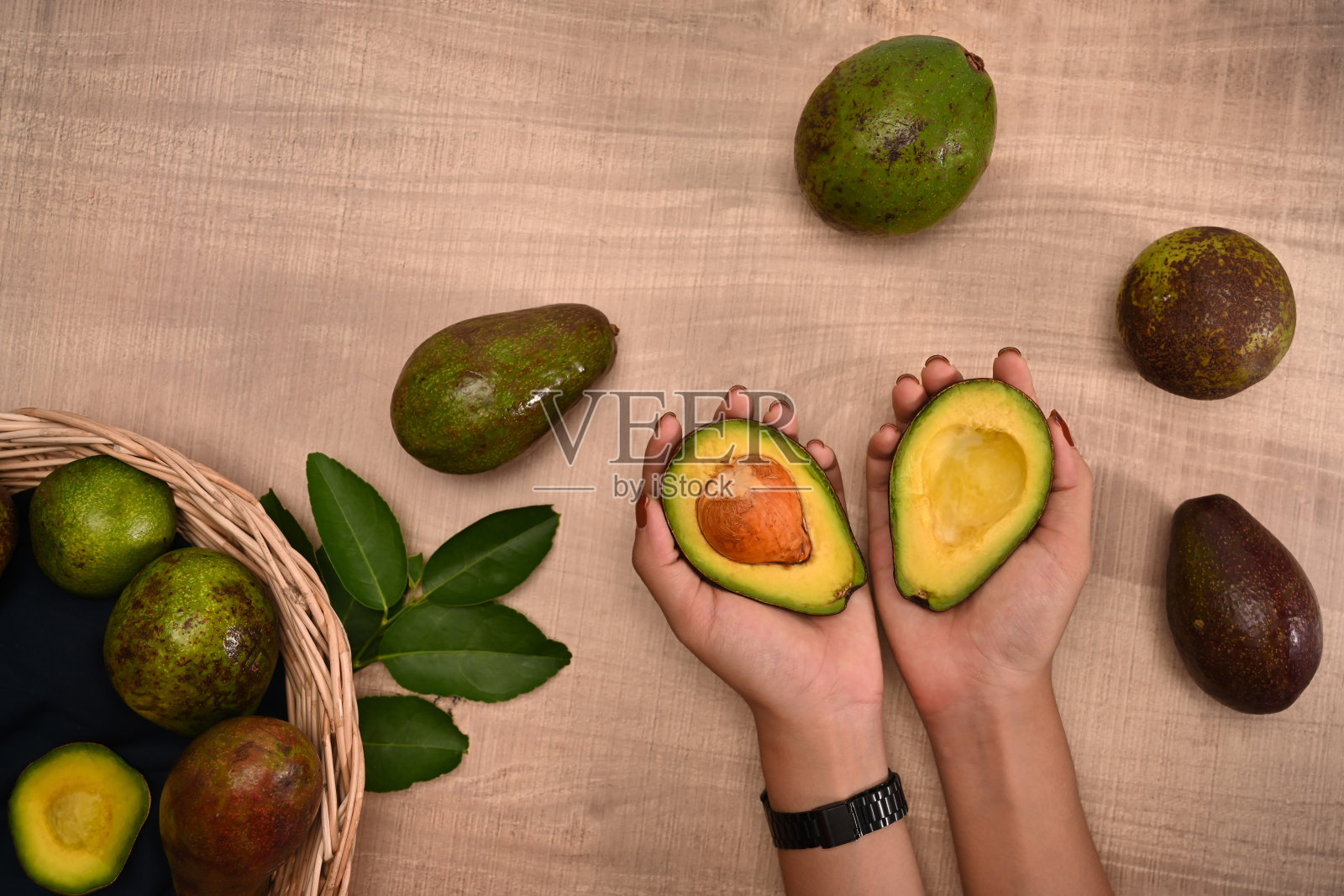 女性拿着新鲜的鳄梨在木头背景上。照片摄影图片