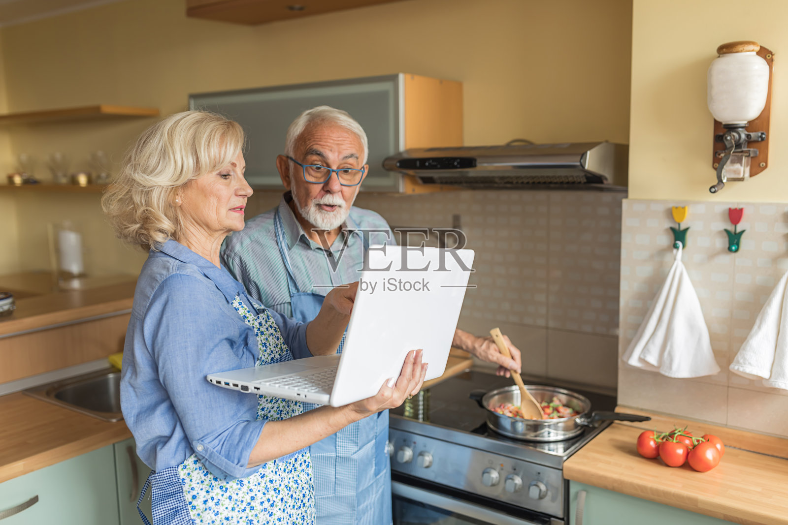 幸福的老女人和她的丈夫正在度过一个美好的时间,同时享受在家里准备晚餐。一位女士正在用笔记本电脑寻找最佳食谱。照片摄影图片