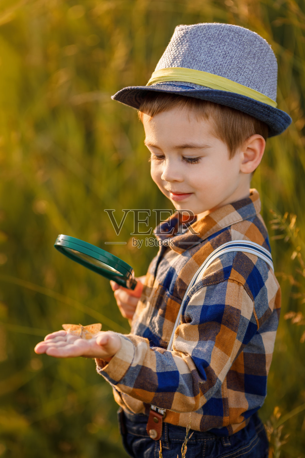 小男孩拿着放大镜在草地上探索大自然照片摄影图片