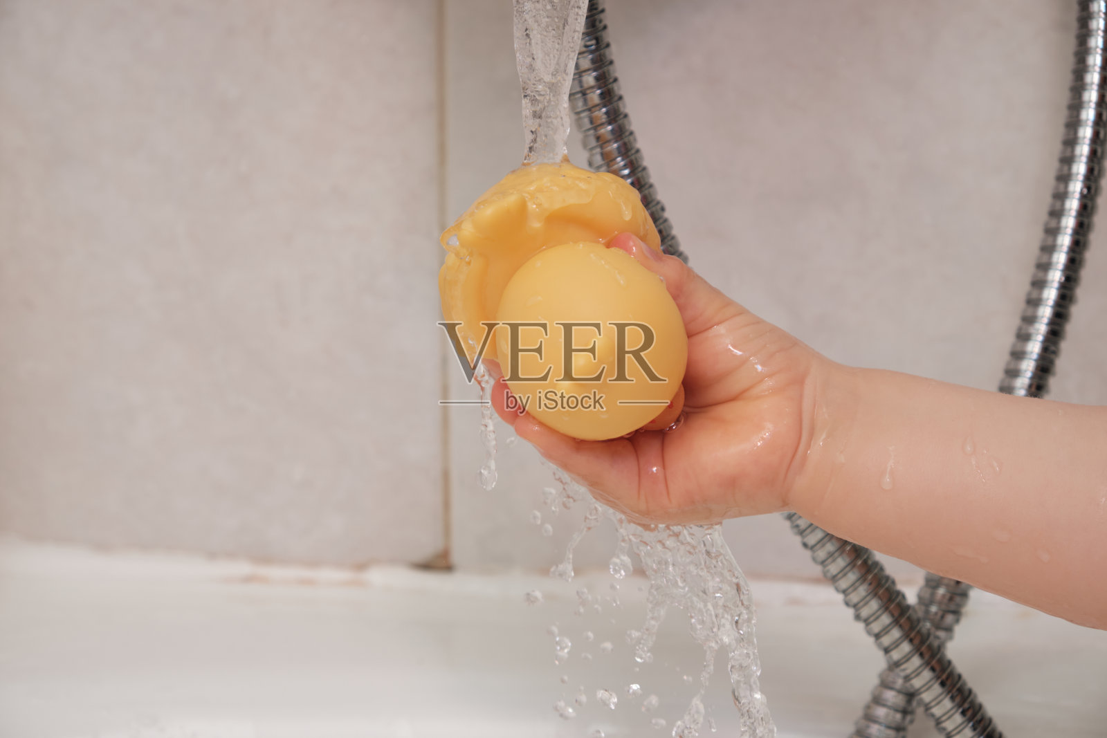 婴儿抱着一只橡皮鸭在浴缸龙头下倒水照片摄影图片