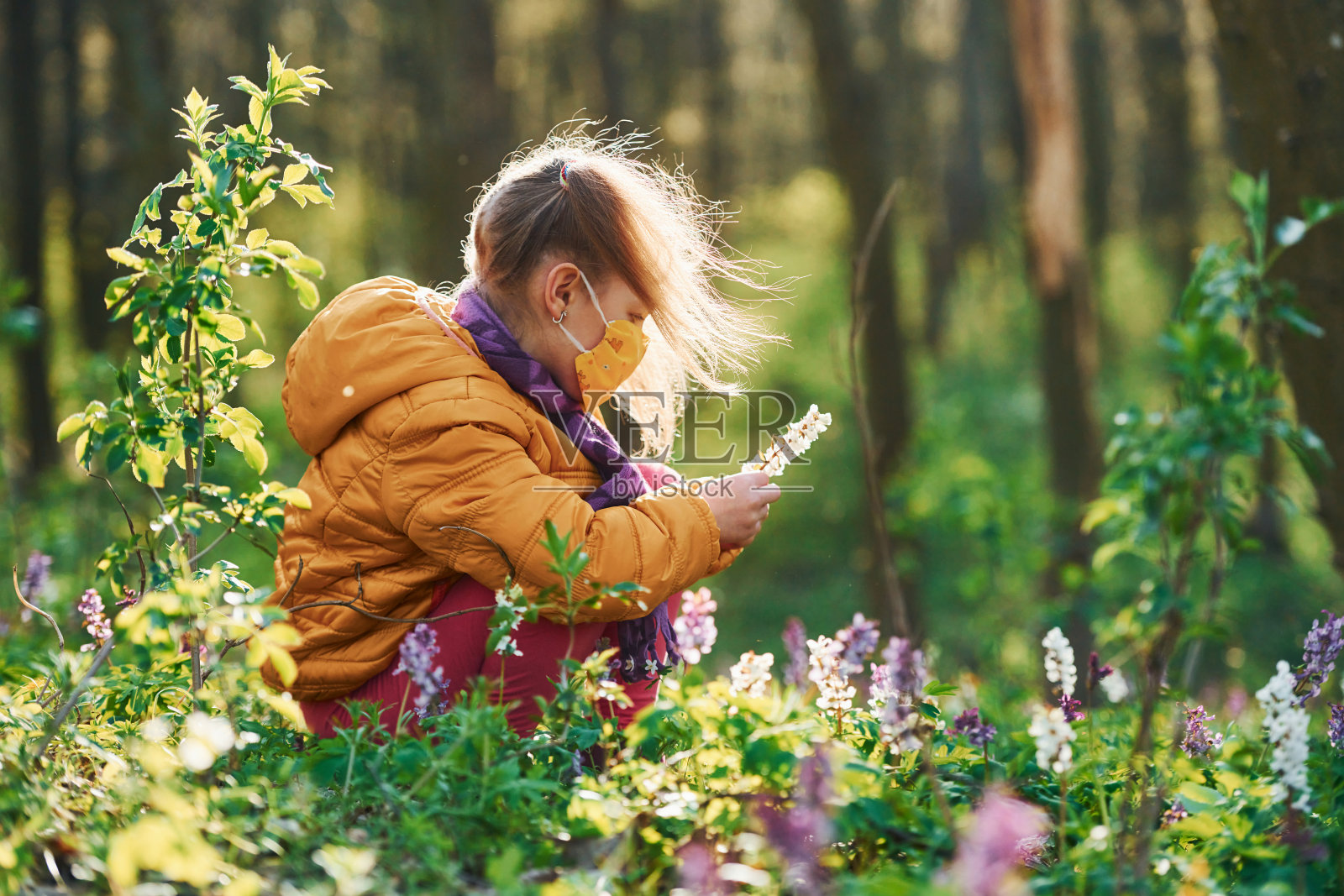 白天,快乐的小女孩戴着防护面具坐在春天的森林里照片摄影图片