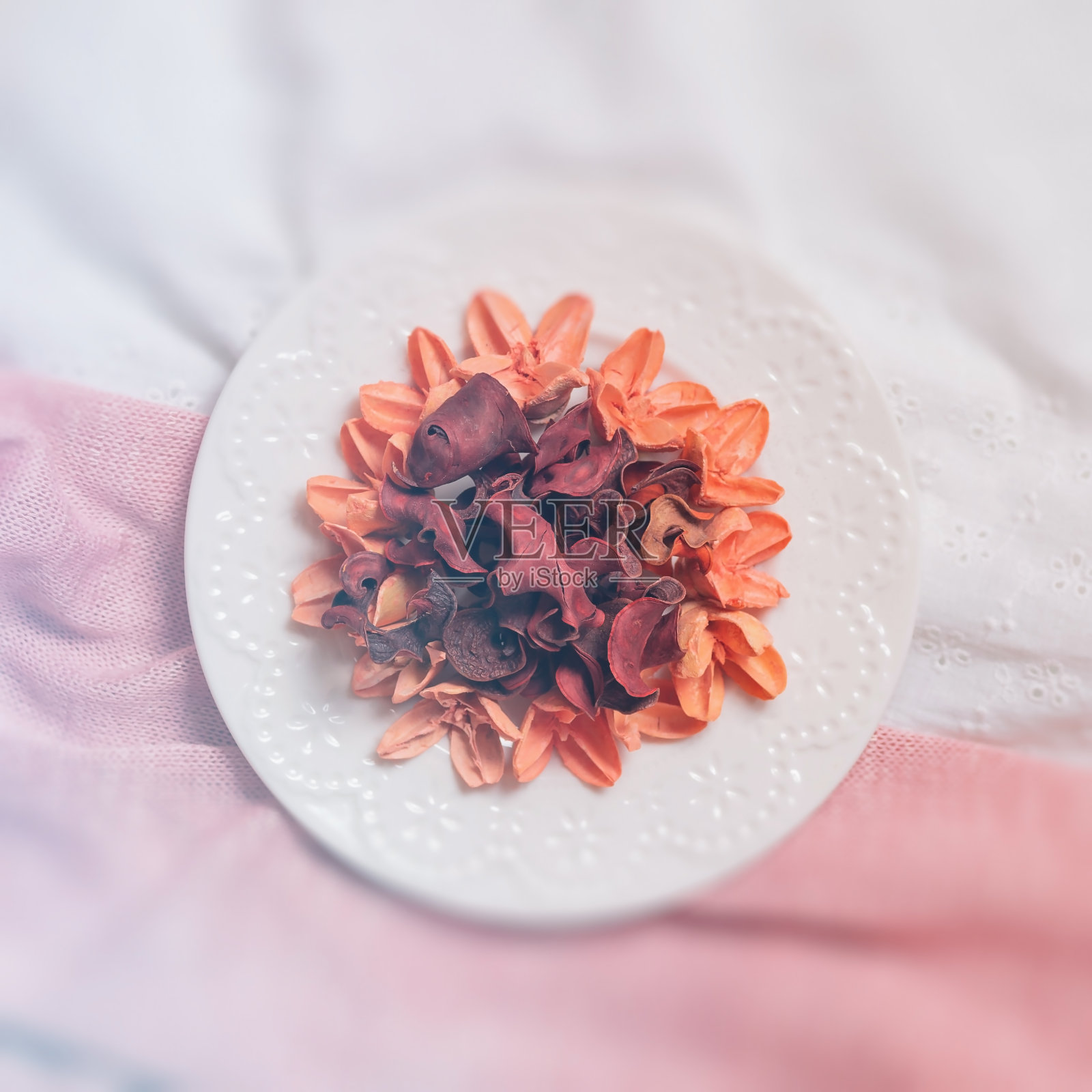 粉红色织物上有干花和花瓣的盘子。照片摄影图片