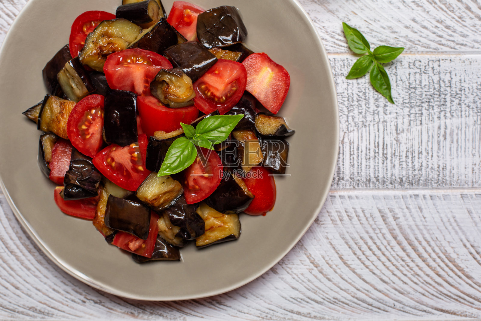 特写烤茄子与新鲜的西红柿和罗勒叶。光背景。照片摄影图片