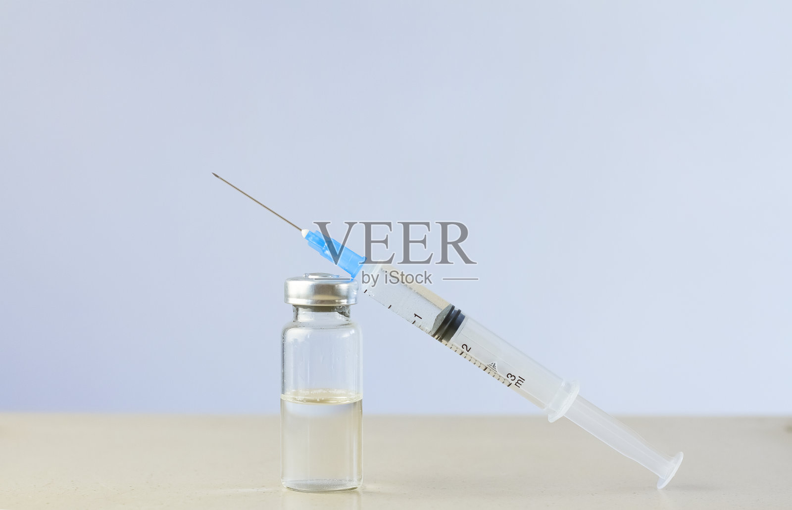 桌上有一支装有透明液体的玻璃安瓿,还有一支注射器。注射器在安瓿旁。照片摄影图片