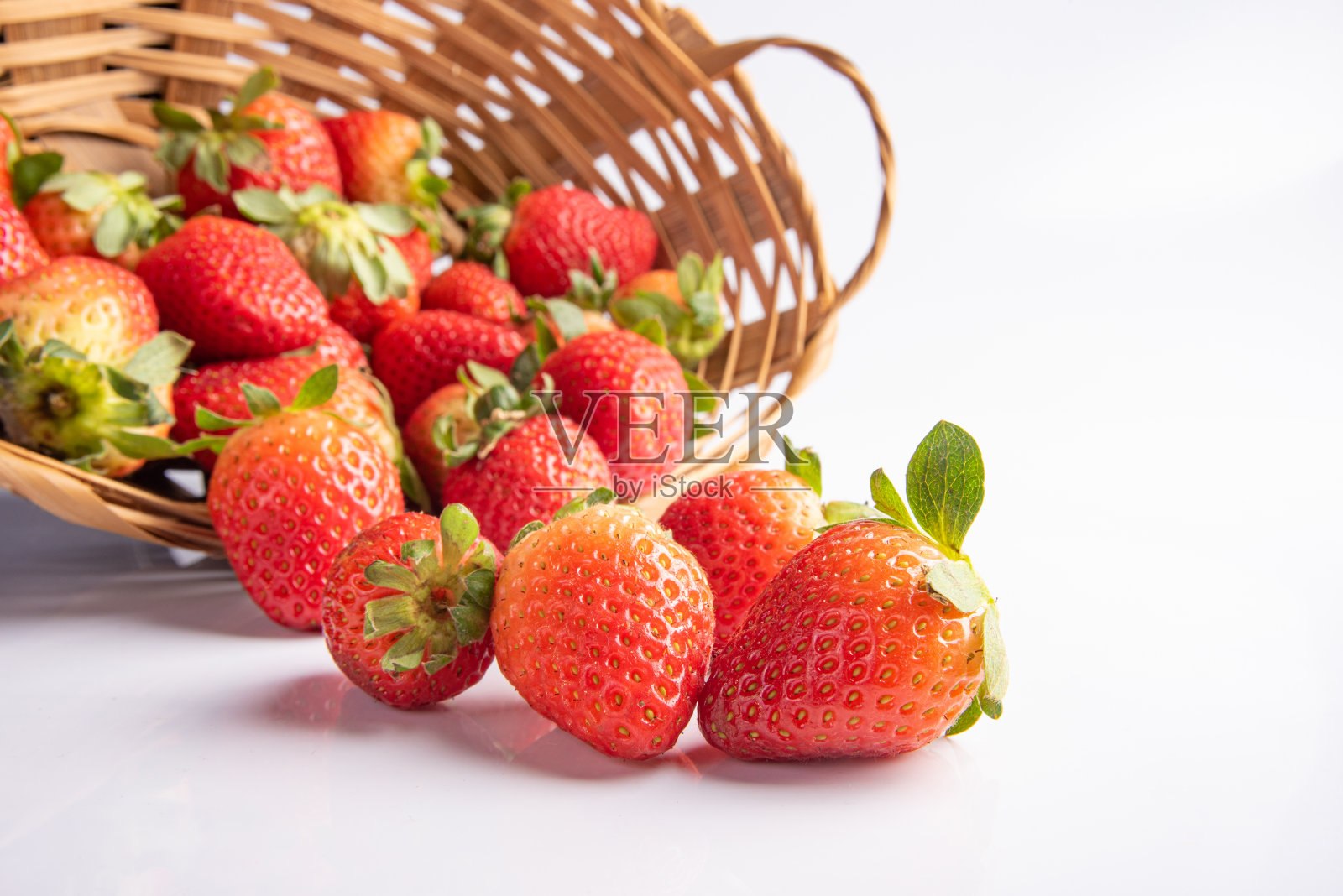 草莓,漂亮的草莓从稻草编织的篮子里掉落到白色的表面上,选择性的聚焦。照片摄影图片