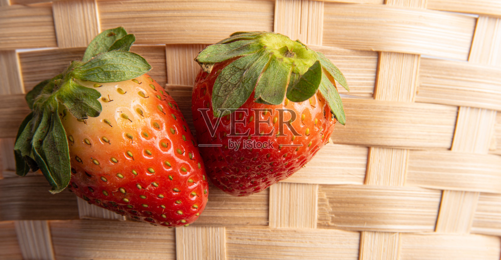 草莓,两个漂亮的草莓放在编织的草篮上,有选择性地聚焦。照片摄影图片