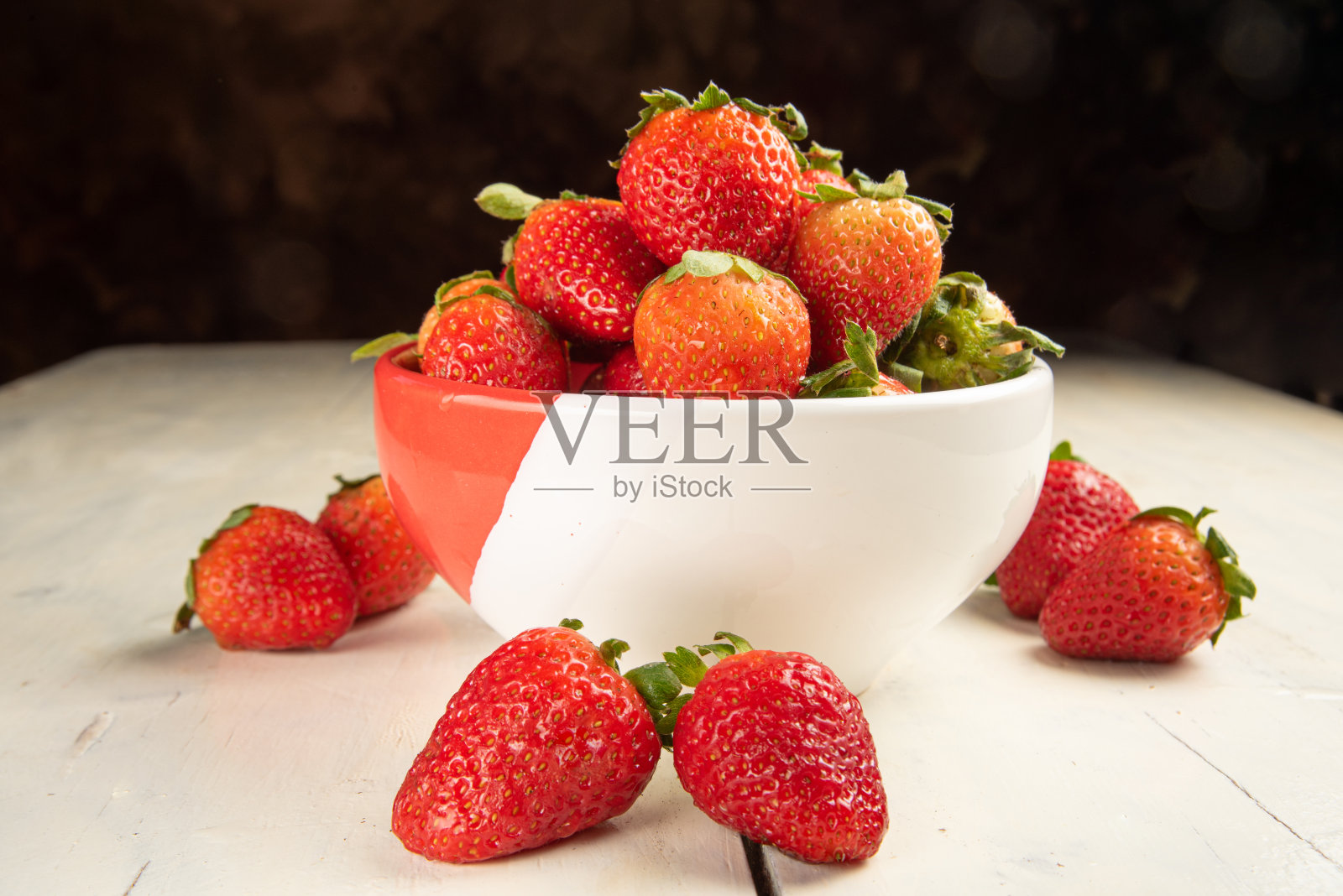 草莓,一碗草莓放在旧的白色桌子上,黑色抽象背景,选择性聚焦。照片摄影图片