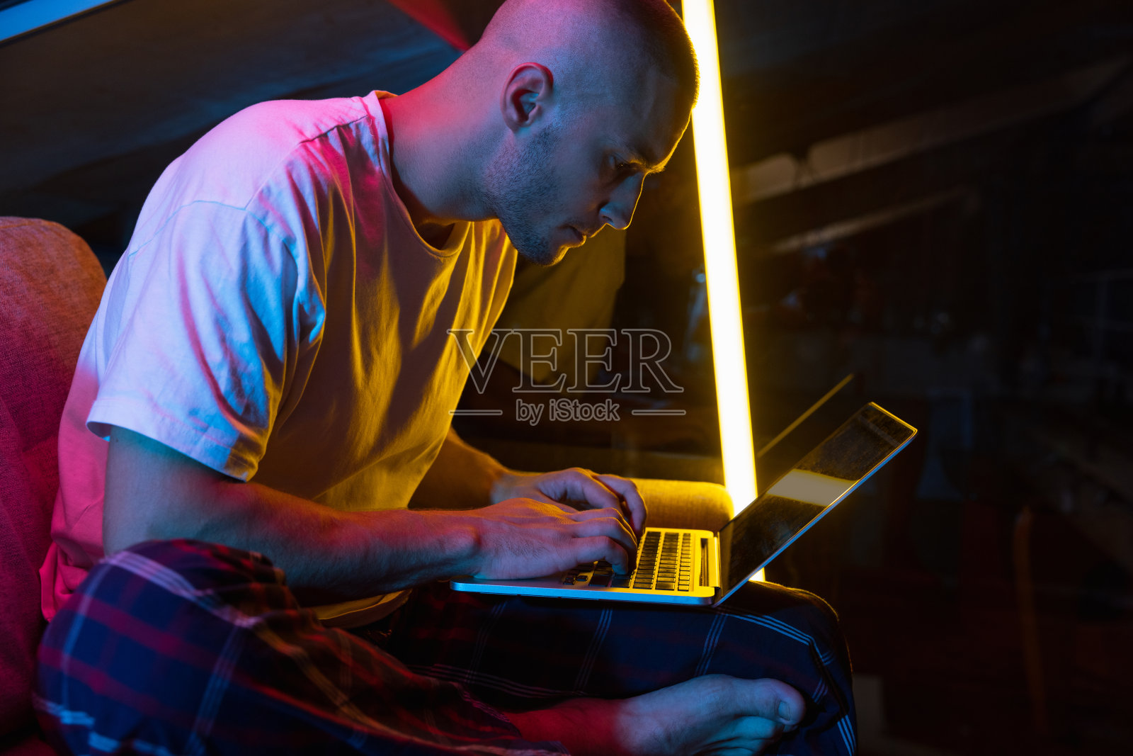 年轻英俊的白人男子的肖像坐在家里的霓虹灯橙色的房间。室内时尚男模。反射效果照片摄影图片