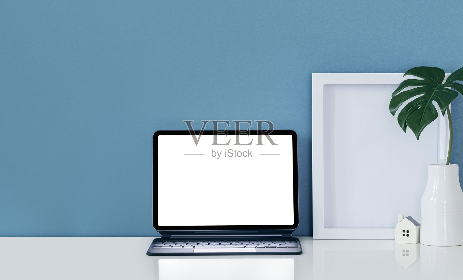 带有魔法键盘、木框和花瓶的平板电脑,白色的桌面和蓝色的墙壁。照片摄影图片
