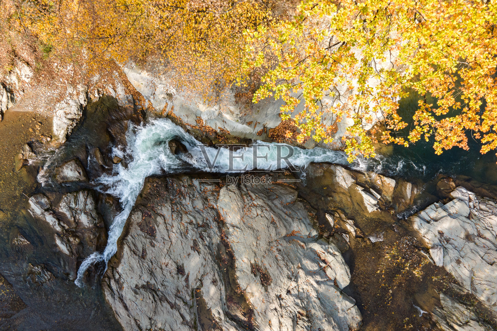 从上到下鸟瞰小山涧与快速移动的清澈的水之间的石头在秋天。照片摄影图片
