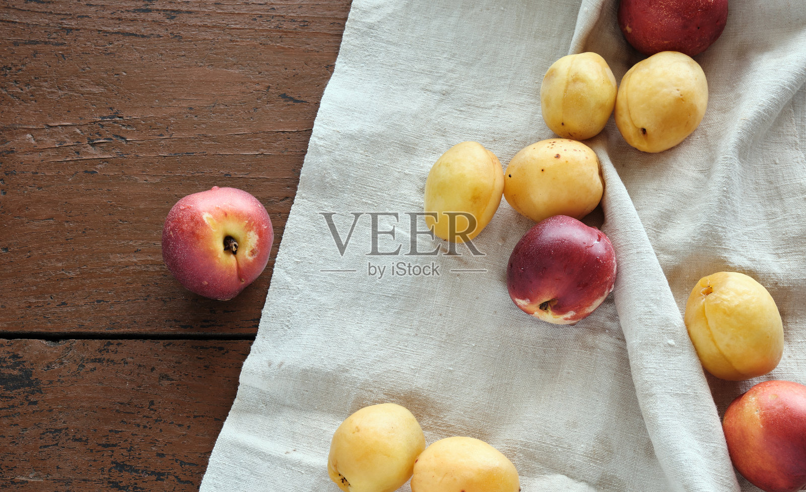 木桌上的亚麻布台布上放着红黄相间的桃子。质朴、简单、环保的风格照片摄影图片