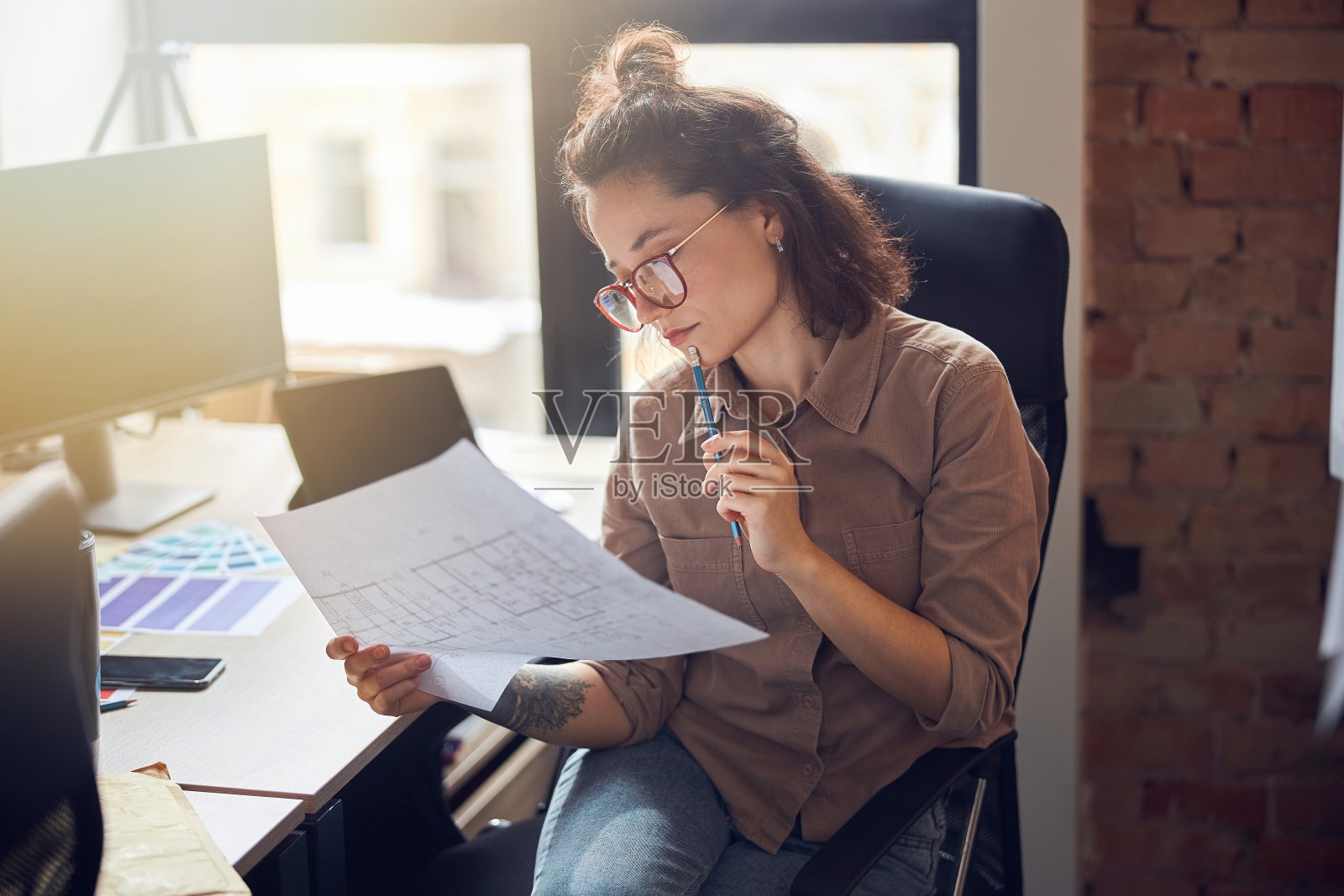 专注于年轻的女性设计师拿着和研究蓝图纸,同时在她的办公室工作新的室内设计项目照片摄影图片