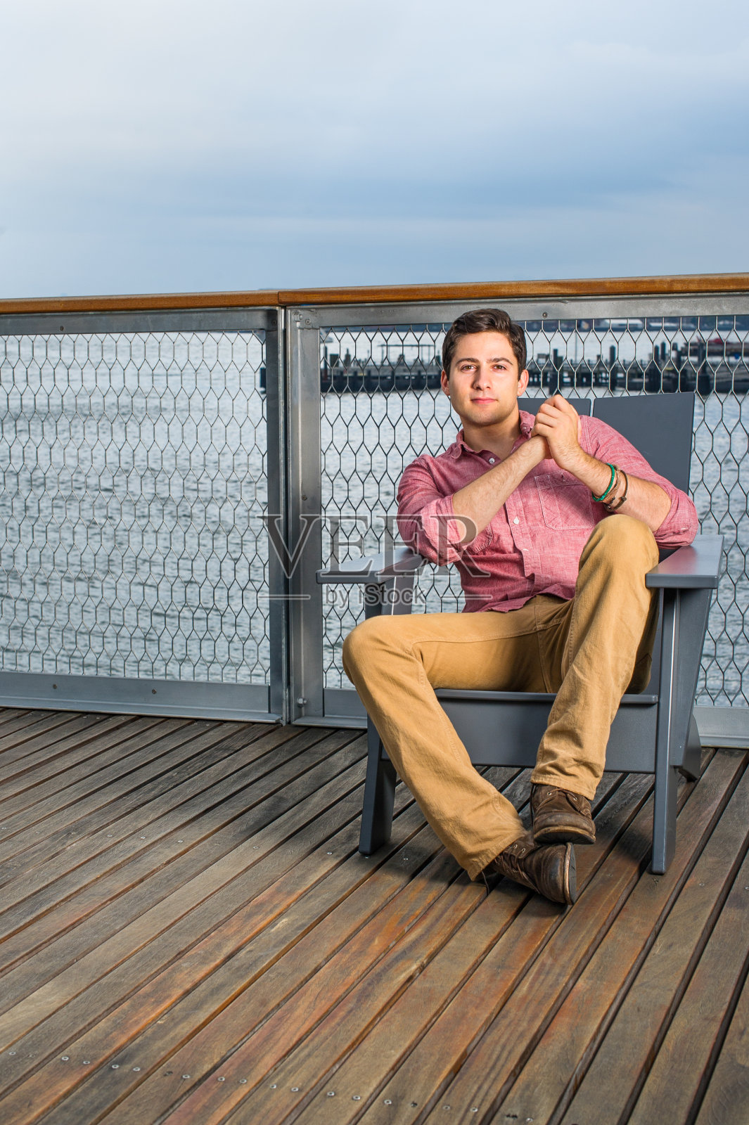 一个年轻人坐在河边甲板上的椅子上,放松着。照片摄影图片