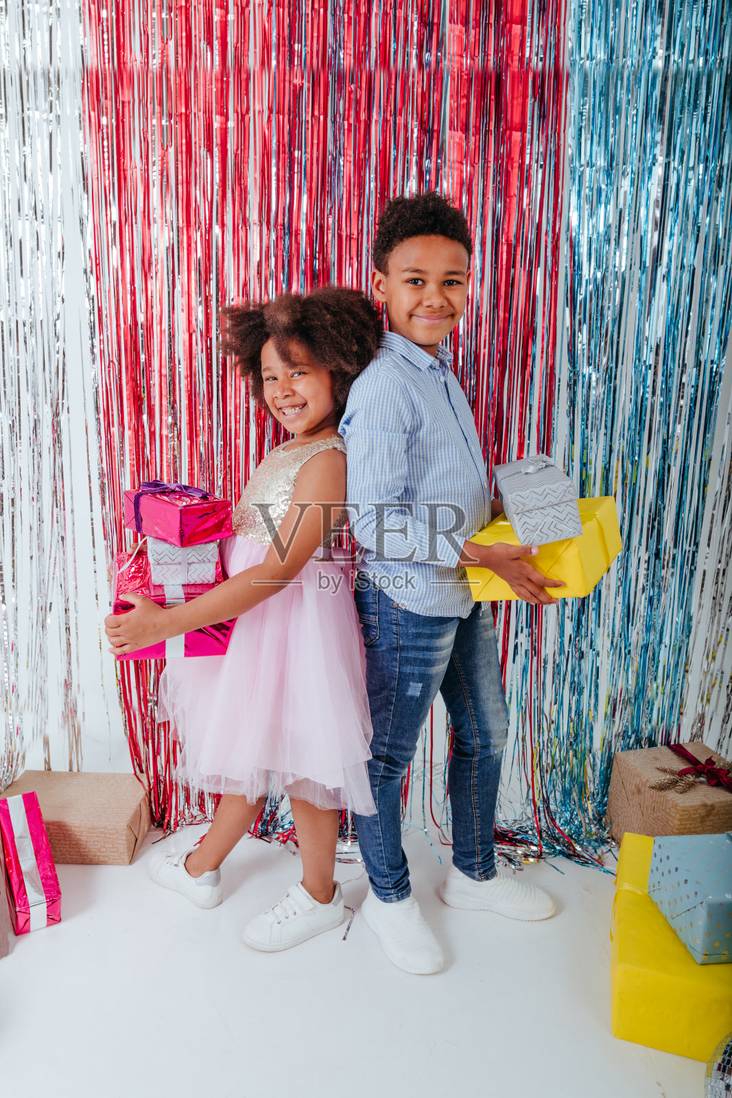快乐的女孩和男孩站在铝箔窗帘旁边,拿着礼物盒照片摄影图片