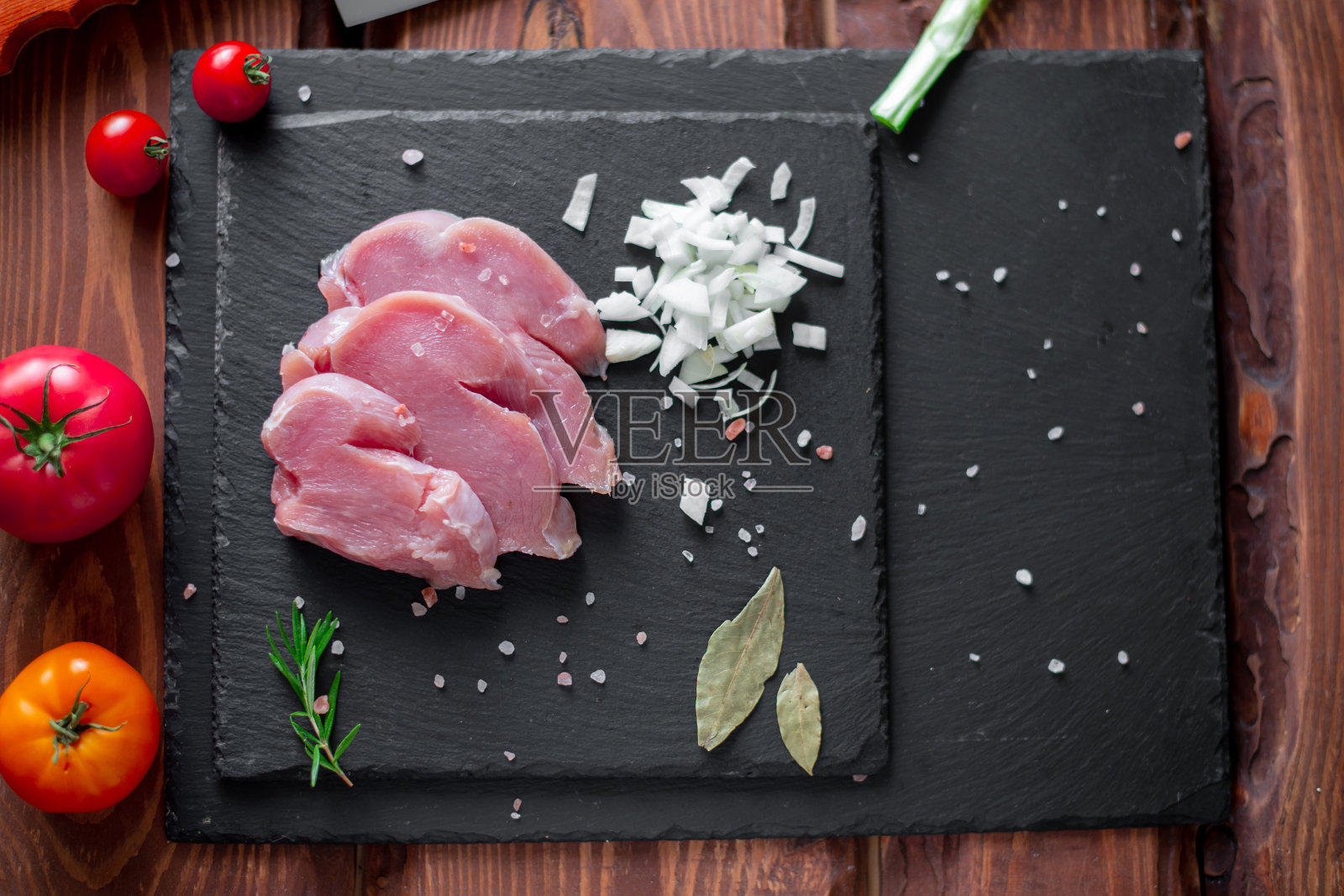 大块的生火鸡肉,切碎的洋葱,在黑色石板的背景上。照片摄影图片