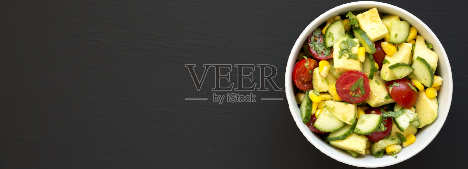 新鲜牛油果西红柿沙拉在一个黑色的碗表面,俯视图。平躺着,从上面俯视。副本的空间。照片摄影图片