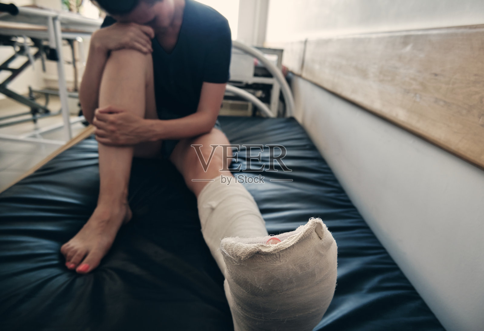 一个断腿的女人坐在医院的沙发上,懊悔不已。腿受伤。失去流动性。骨折后的康复照片摄影图片
