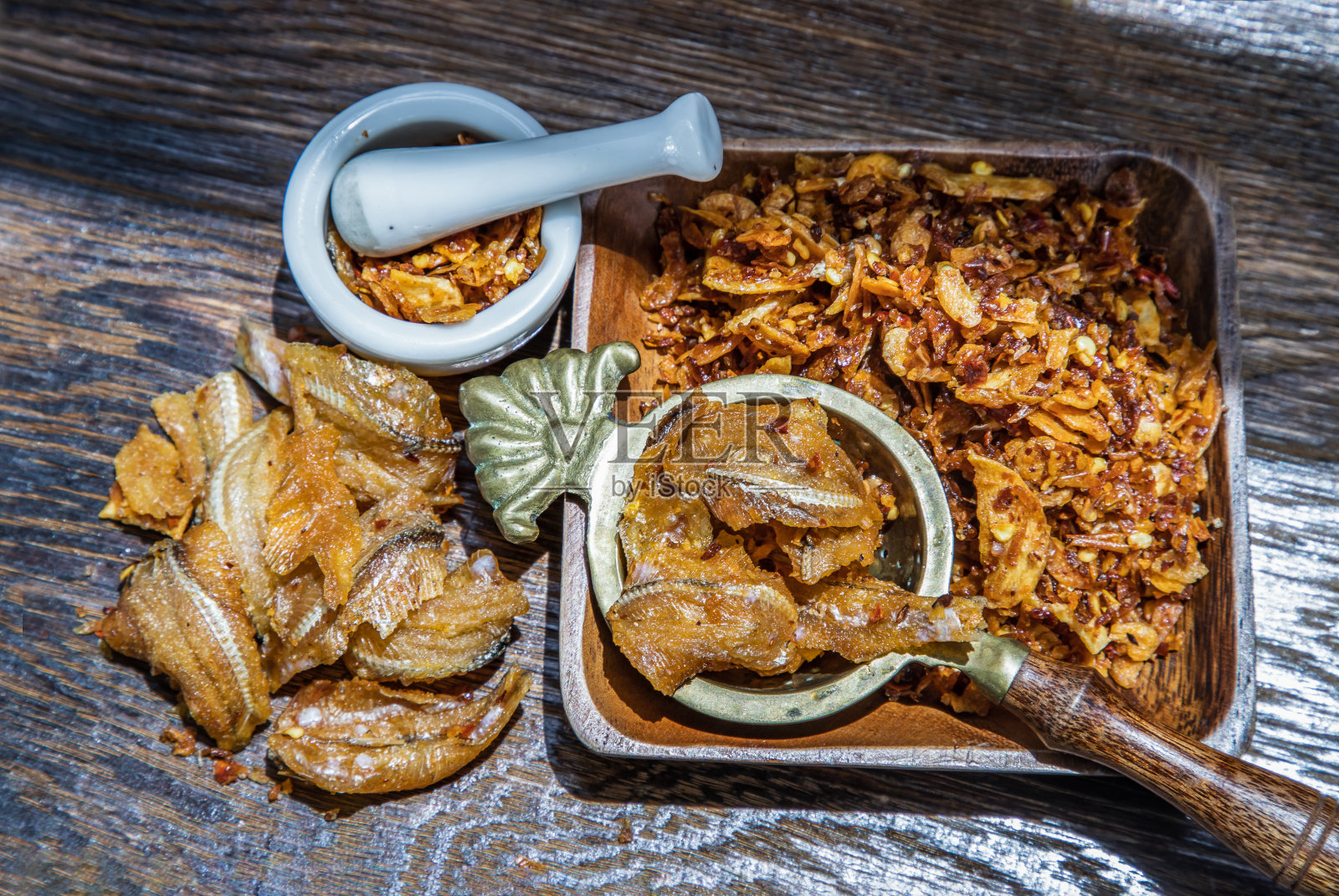 泰式香脆鱼干辣椒酱或香脆鱼辣椒酱放在陶瓷白色的杯子里,放在木桌上。照片摄影图片