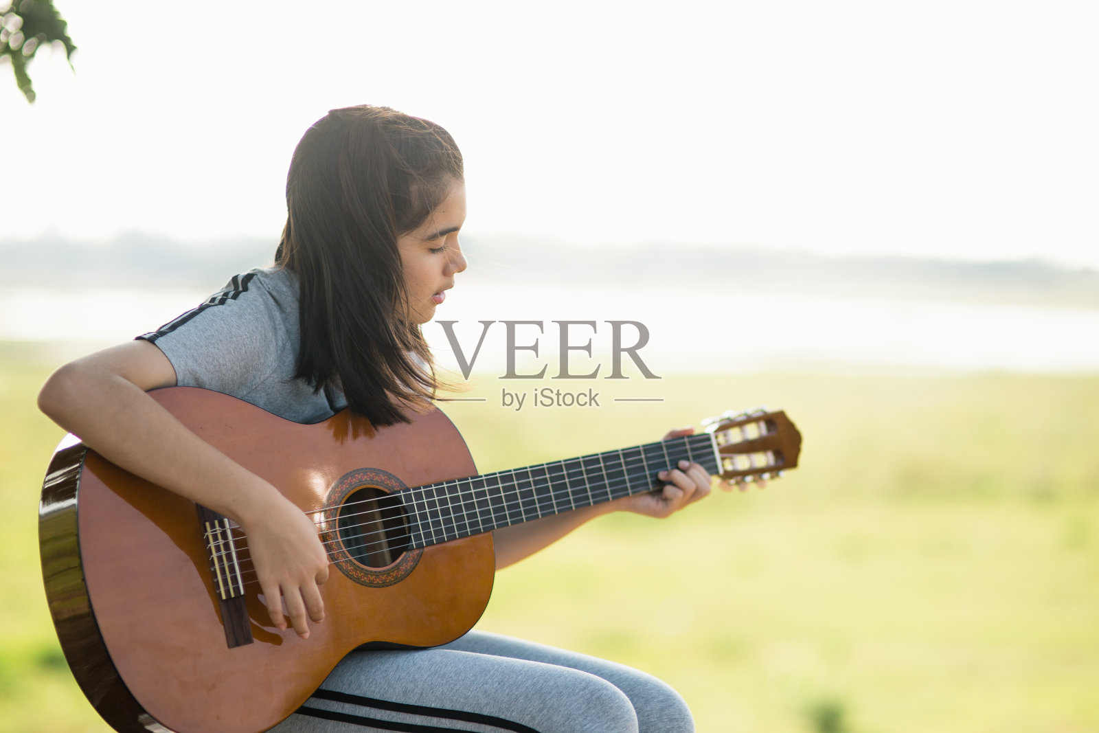 可爱的女孩,弹吉他,唱歌,音乐或幸福概念,日落温暖的光色调效果。照片摄影图片