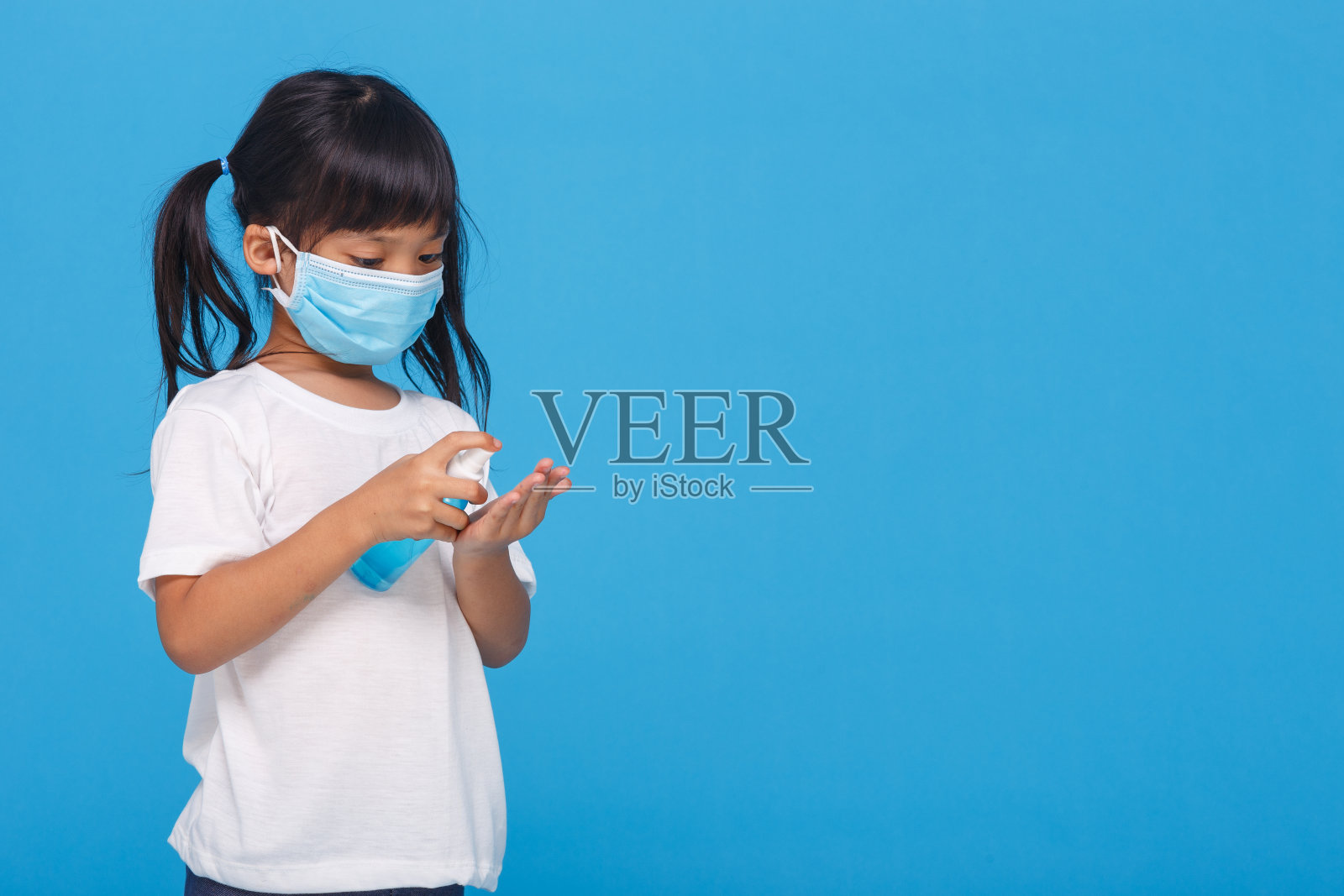 可爱的亚洲女孩戴着口罩,用酒精洗手,以防止在白色背景下传播疾病。预防流感病毒传播照片摄影图片