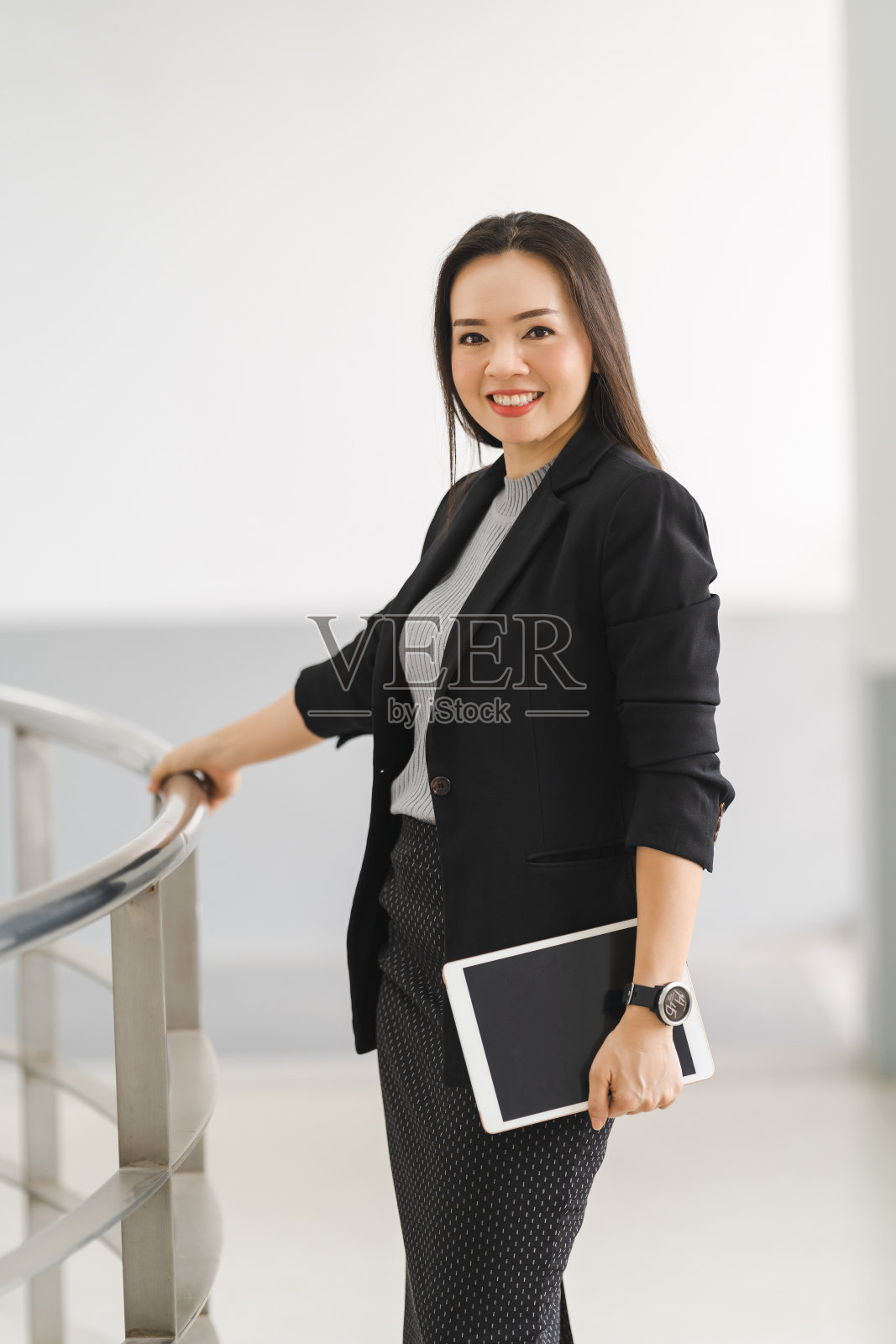 这是一幅乐观自信的亚洲女商人的肖像,她穿着商务套装,站在办公大楼里使用数码平板电脑。商业库存图片照片摄影图片