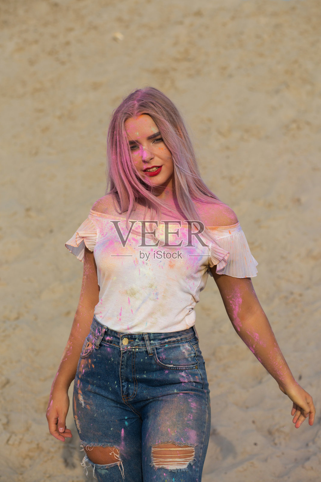 漂亮的金发女人穿着白色t恤和牛仔裤,在沙漠里玩着粉红色的胡里节油漆照片摄影图片