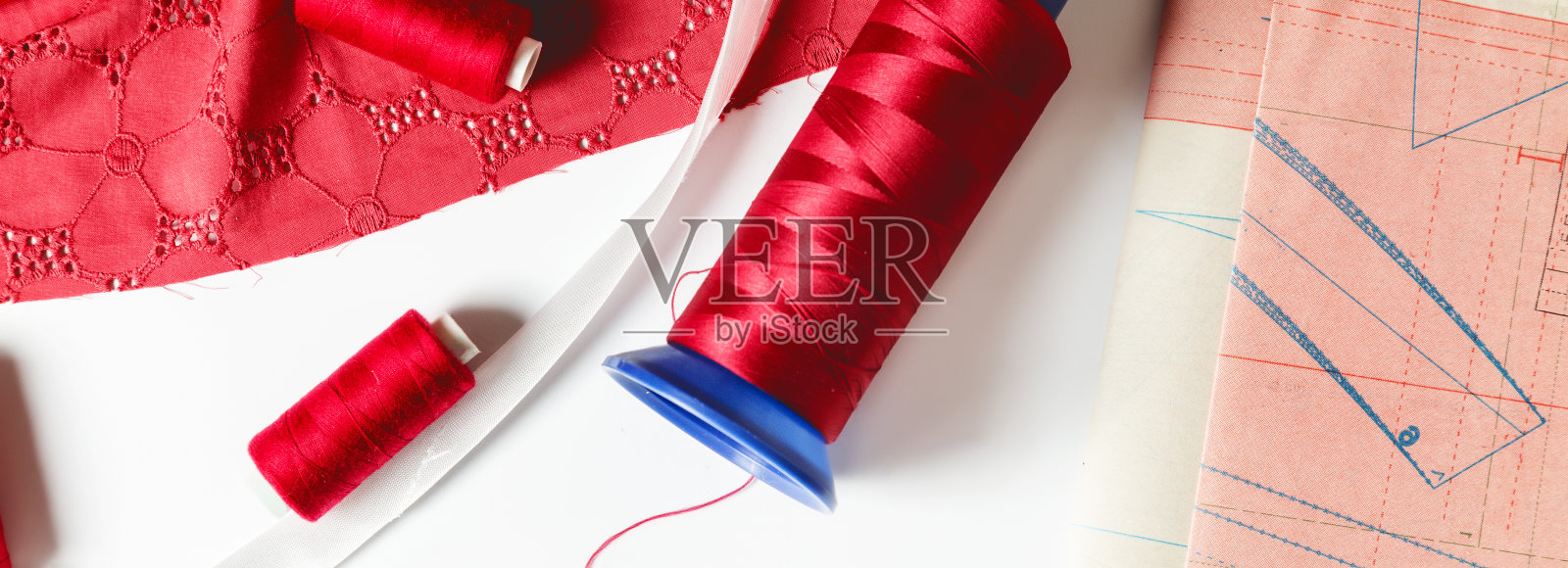 服装设计。成衣及时装收集处,裁缝处。衣服和缝纫工具的图案。红布,线,线轴,白色背景。横幅照片摄影图片