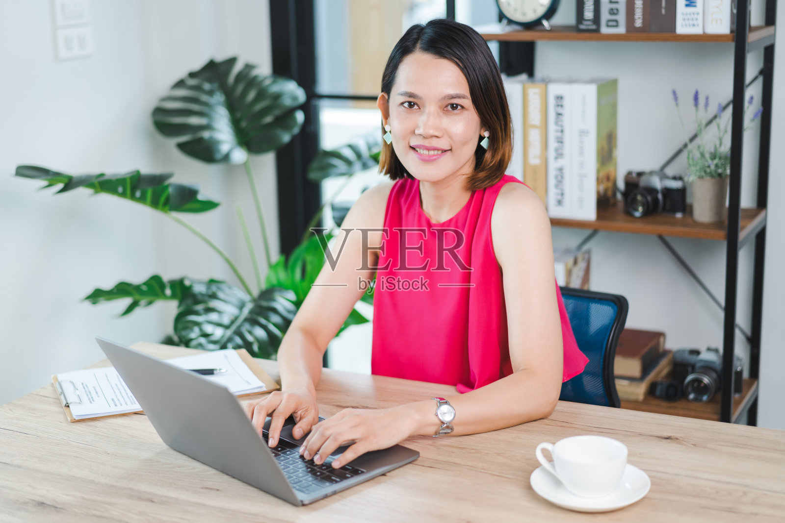 一位快乐的中年亚洲女商人,穿着休闲的休闲装在家工作,在电脑上查看电子邮件,在财务会计凭证上写作。商业库存图片照片摄影图片