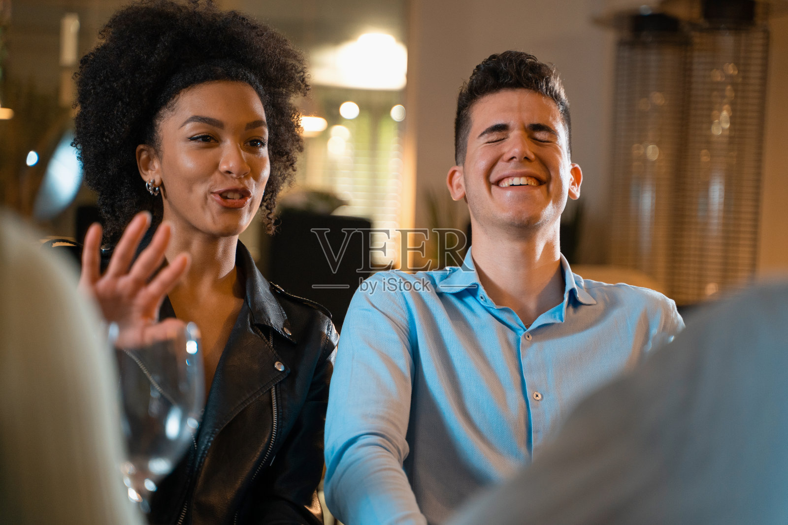 跨种族的人们聚集在餐厅,一起玩乐。年轻夫妇和朋友坐在一起,晚上一起大笑。照片摄影图片