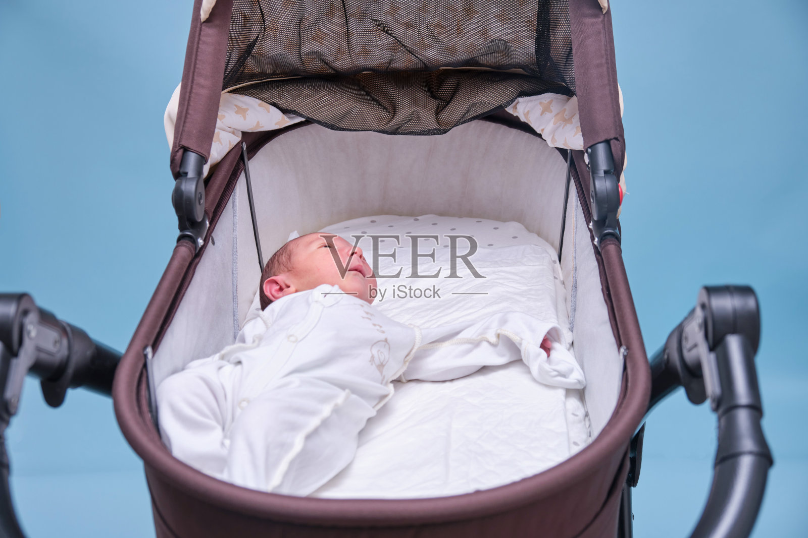 蓝色背景下婴儿车里的小男孩。一个穿着白色衣服只用尿布的孩子躺在婴儿车里,摄影棚拍摄照片摄影图片