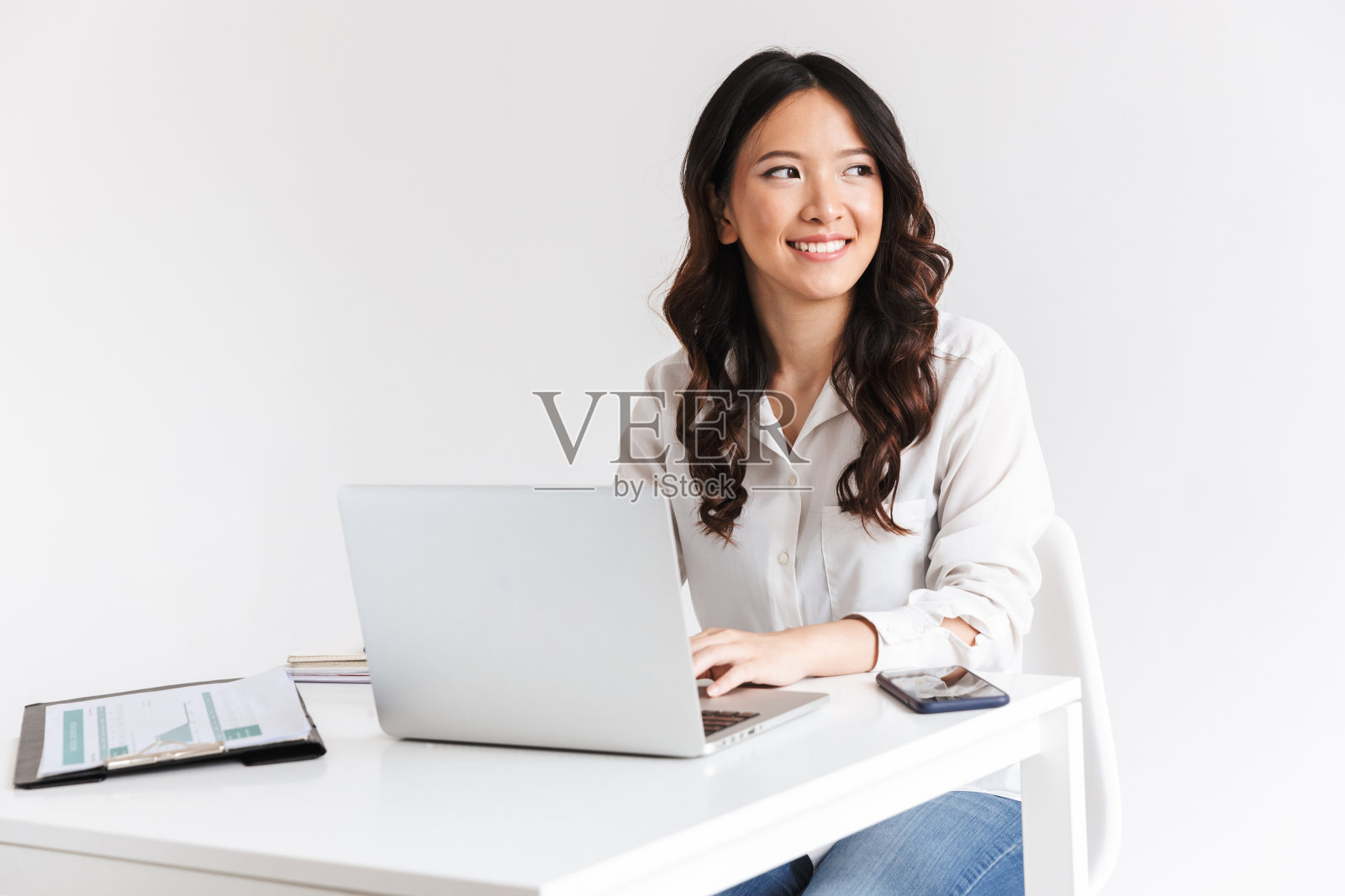 这是一张迷人的中国女商人的照片,她长着黑色的头发,坐在桌子前处理文件和笔记本电脑,在工作室的白色背景下与世隔绝照片摄影图片