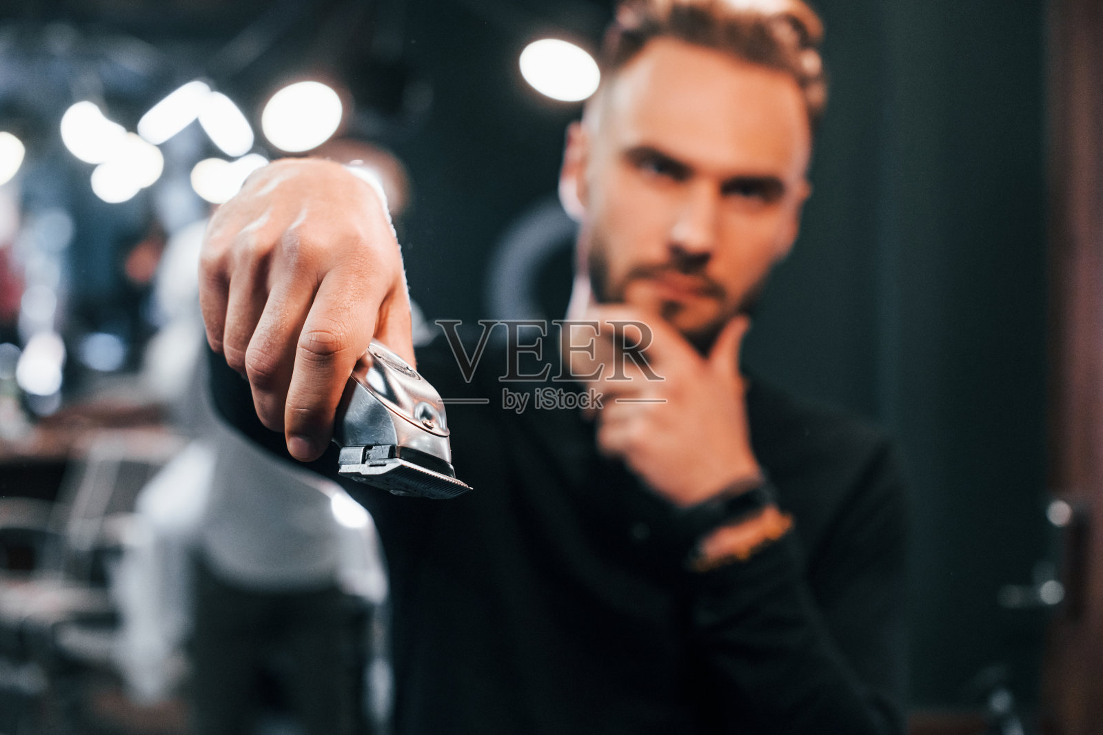 一个留着胡子的年轻人拿着剪子站在理发店里照片摄影图片