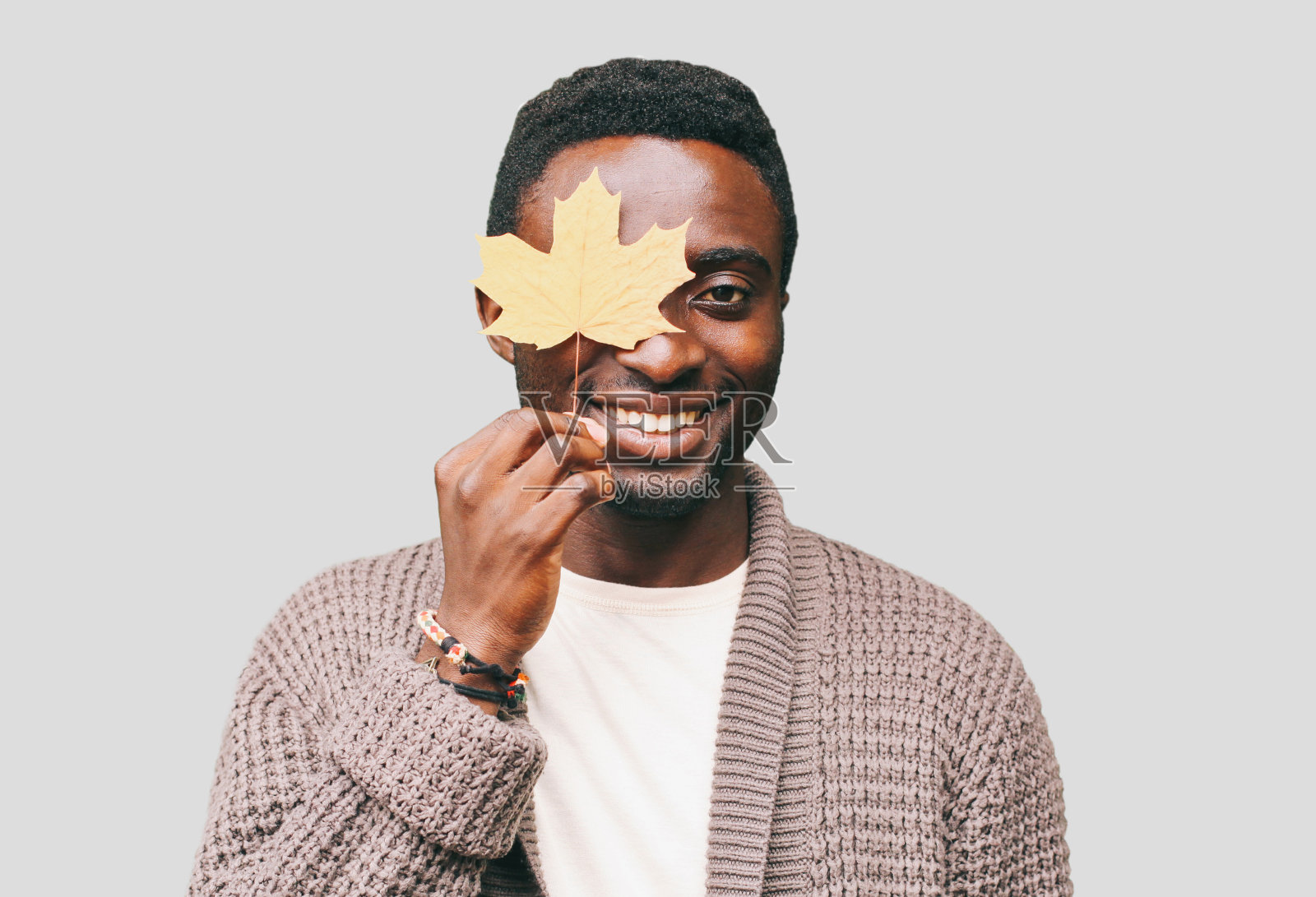 一个快乐微笑的非洲人的肖像与秋天的黄色枫叶在灰色的背景照片摄影图片