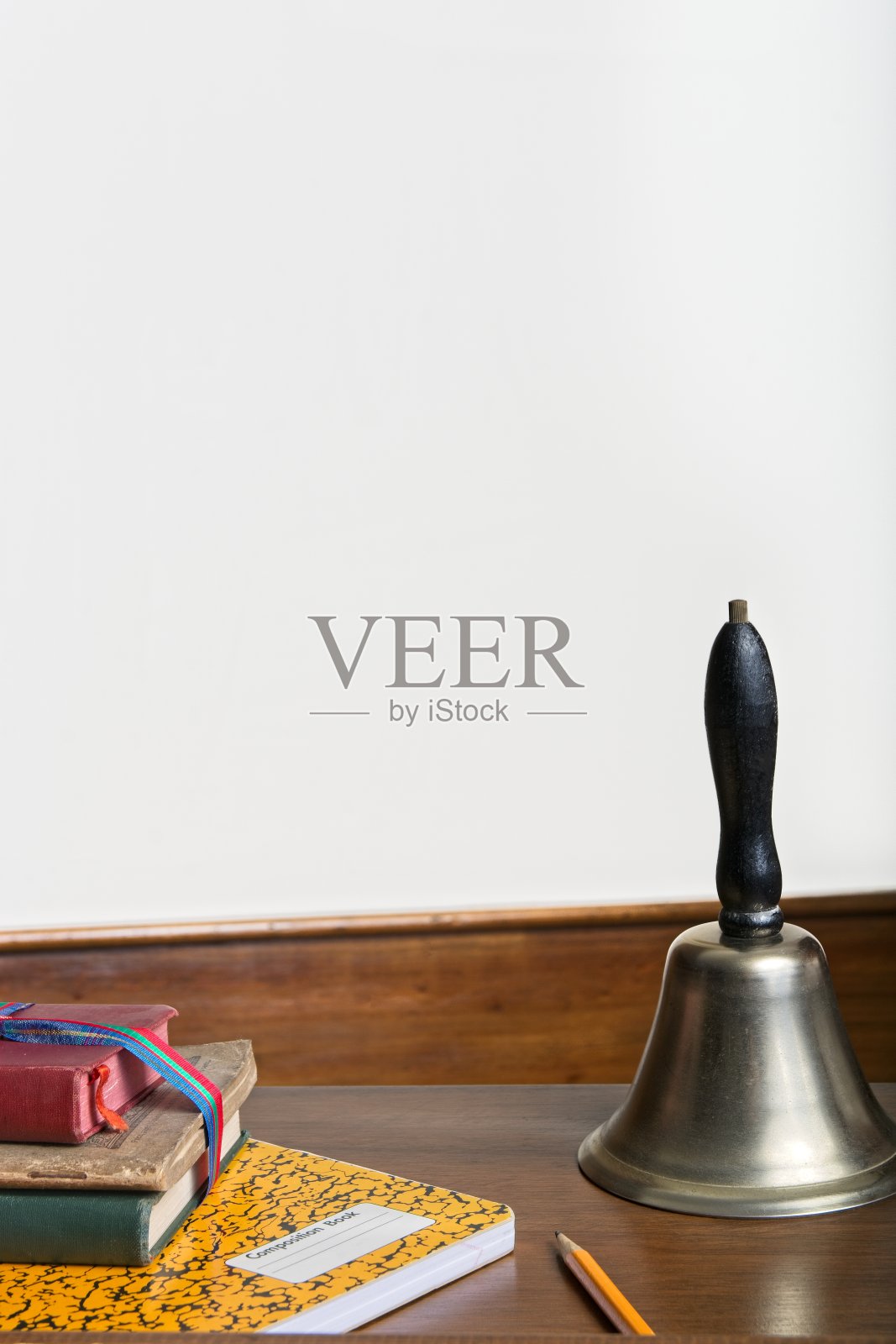 古色古香的课桌概念与教科书、作文书、铅笔和学校手铃摆在巨大的白色墙壁前照片摄影图片