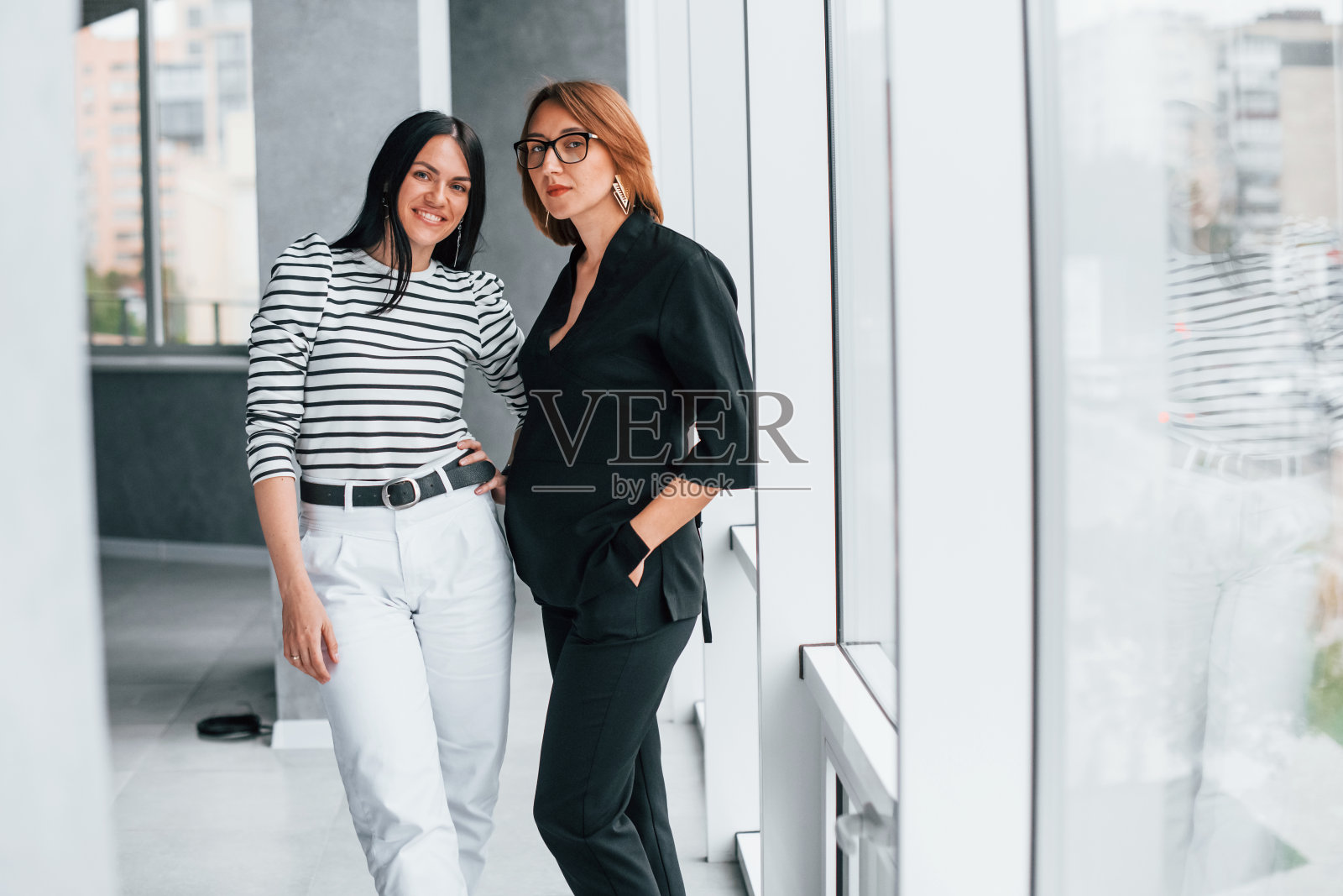 两个女商人一起站在办公室的室内大窗户附近照片摄影图片