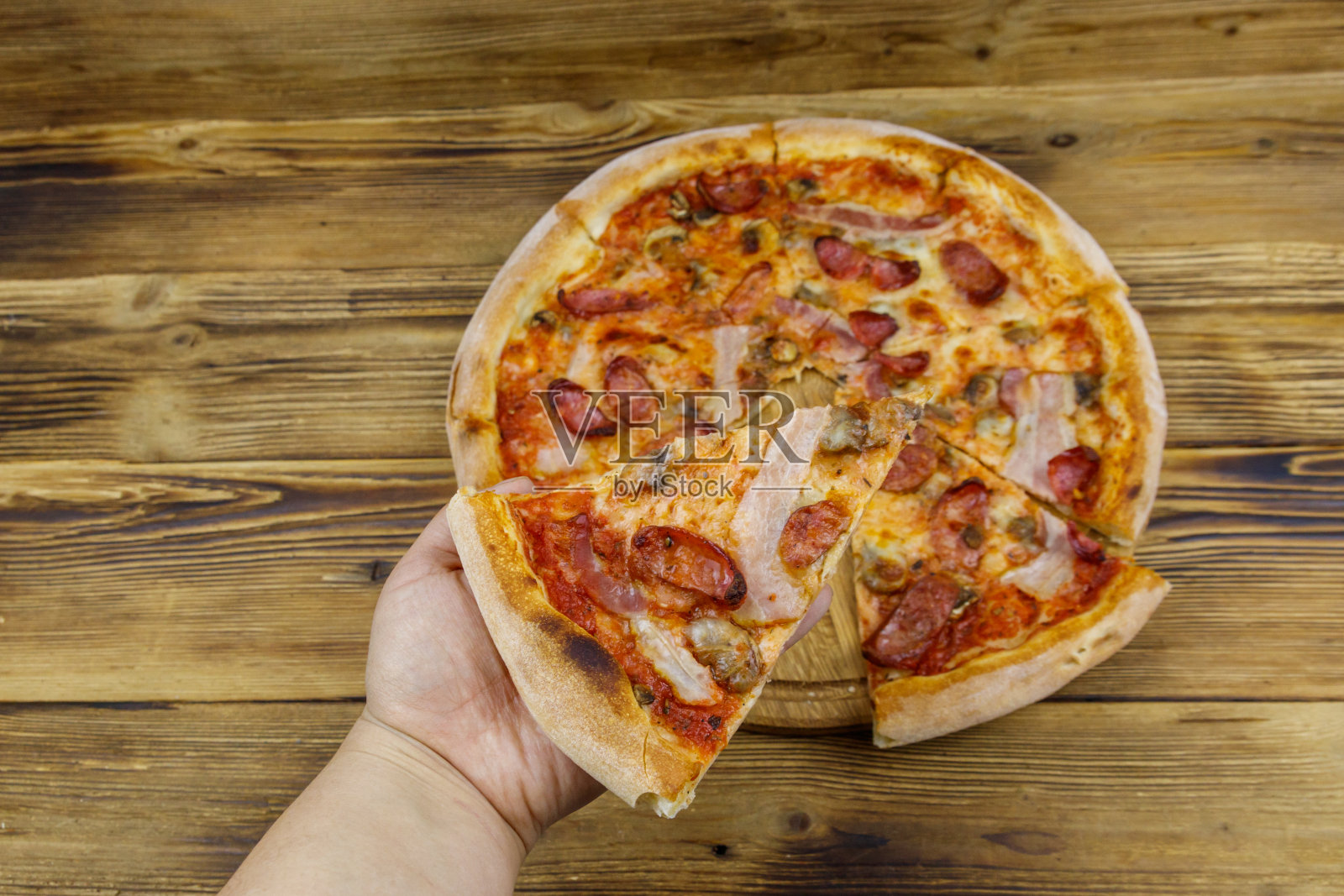 手拿着一片美味的披萨。木桌上放着热意大利披萨。俯视图照片摄影图片