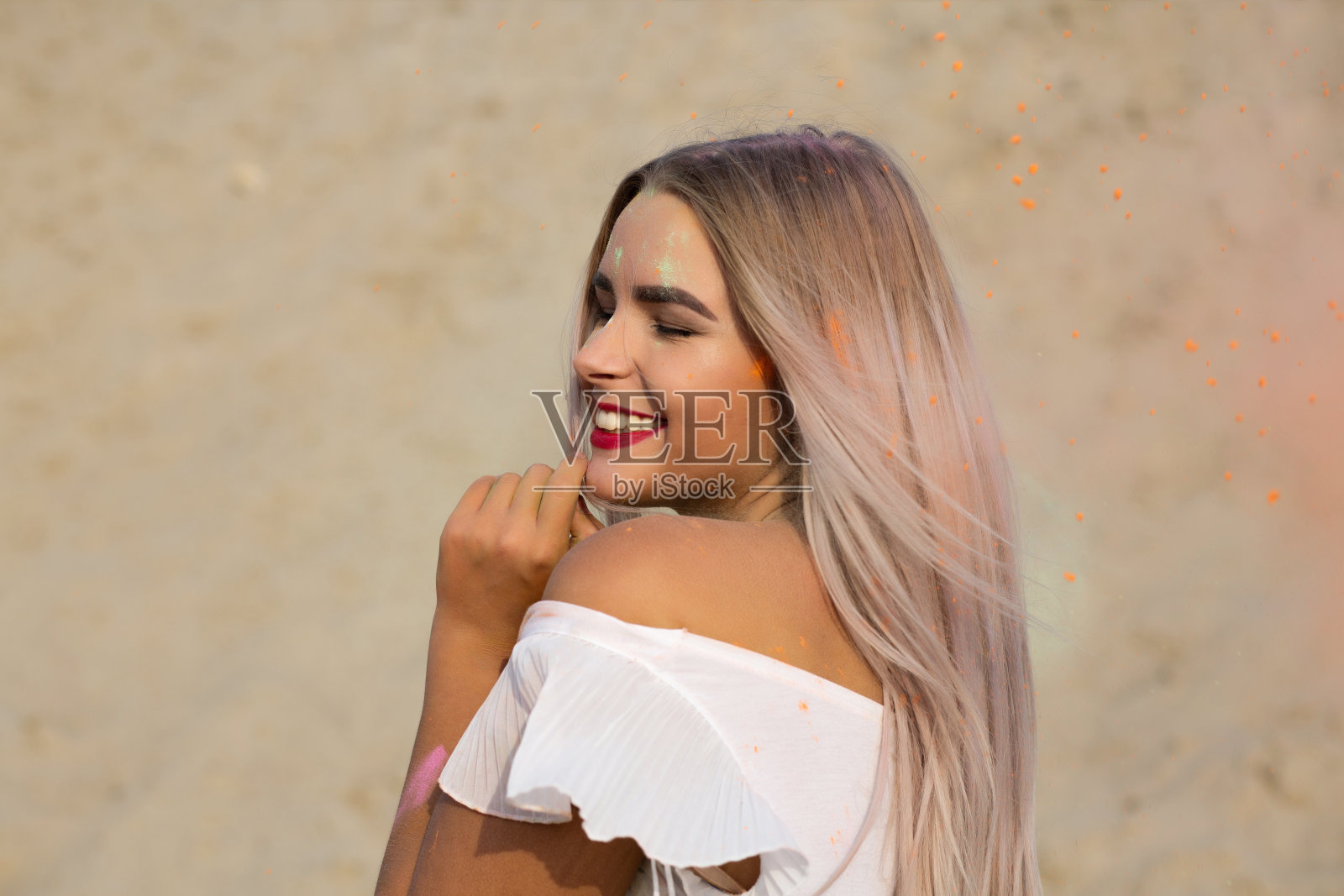 这是一个漂亮的金发女孩的特写镜头,她涂着红色的口红,在沙漠中涂着干颜料照片摄影图片