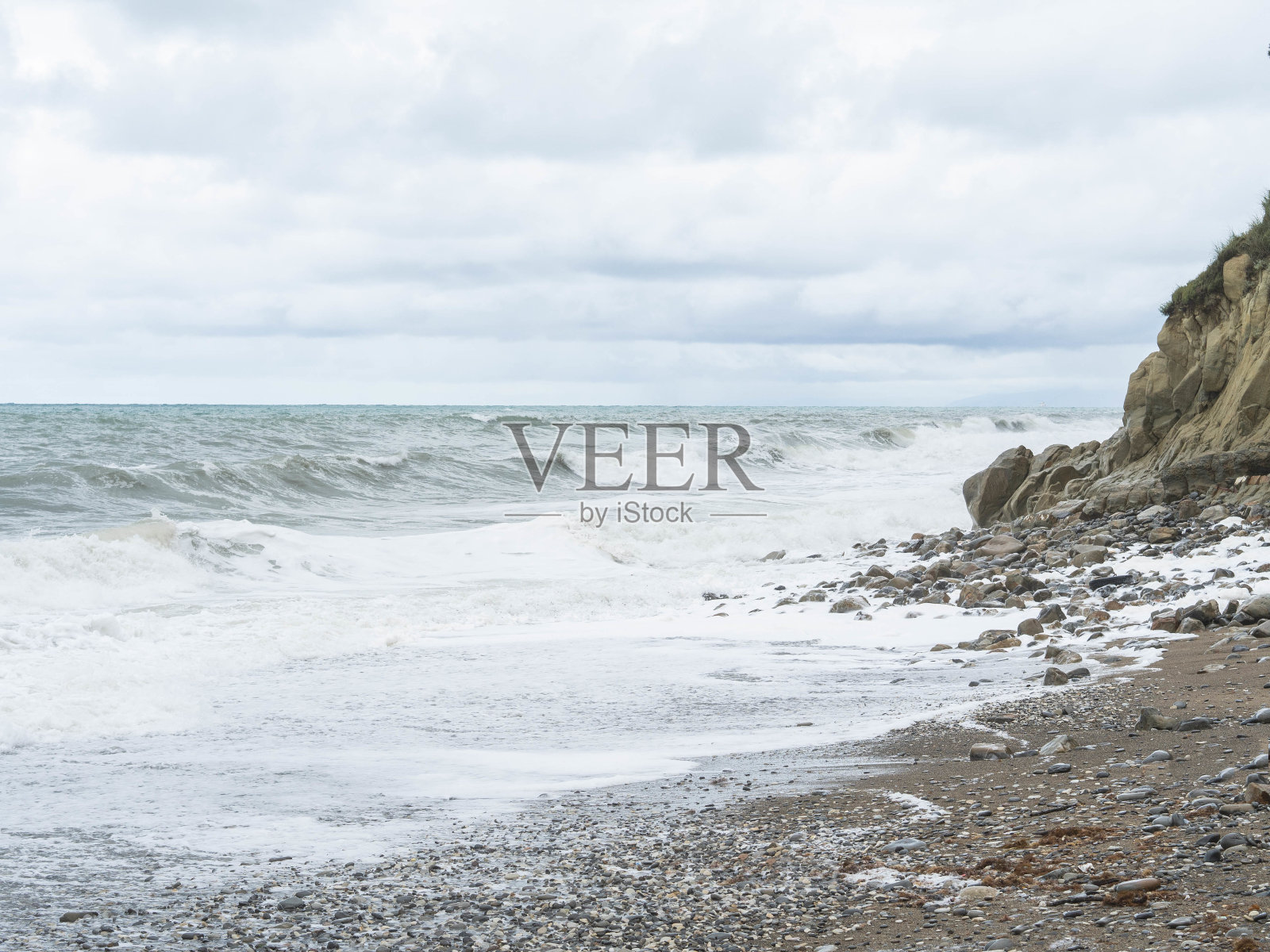 多云的天气里,暴风雨的海浪拍打着石滩。照片摄影图片