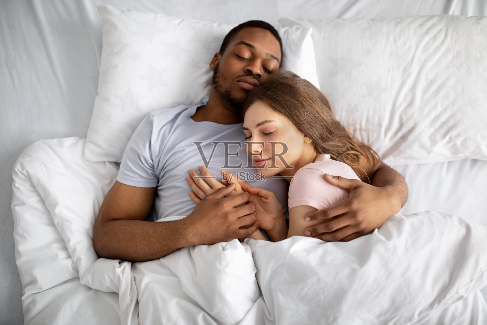 俯视图相爱的跨国夫妇睡在床上,拥抱彼此。多种族关系和婚姻照片摄影图片