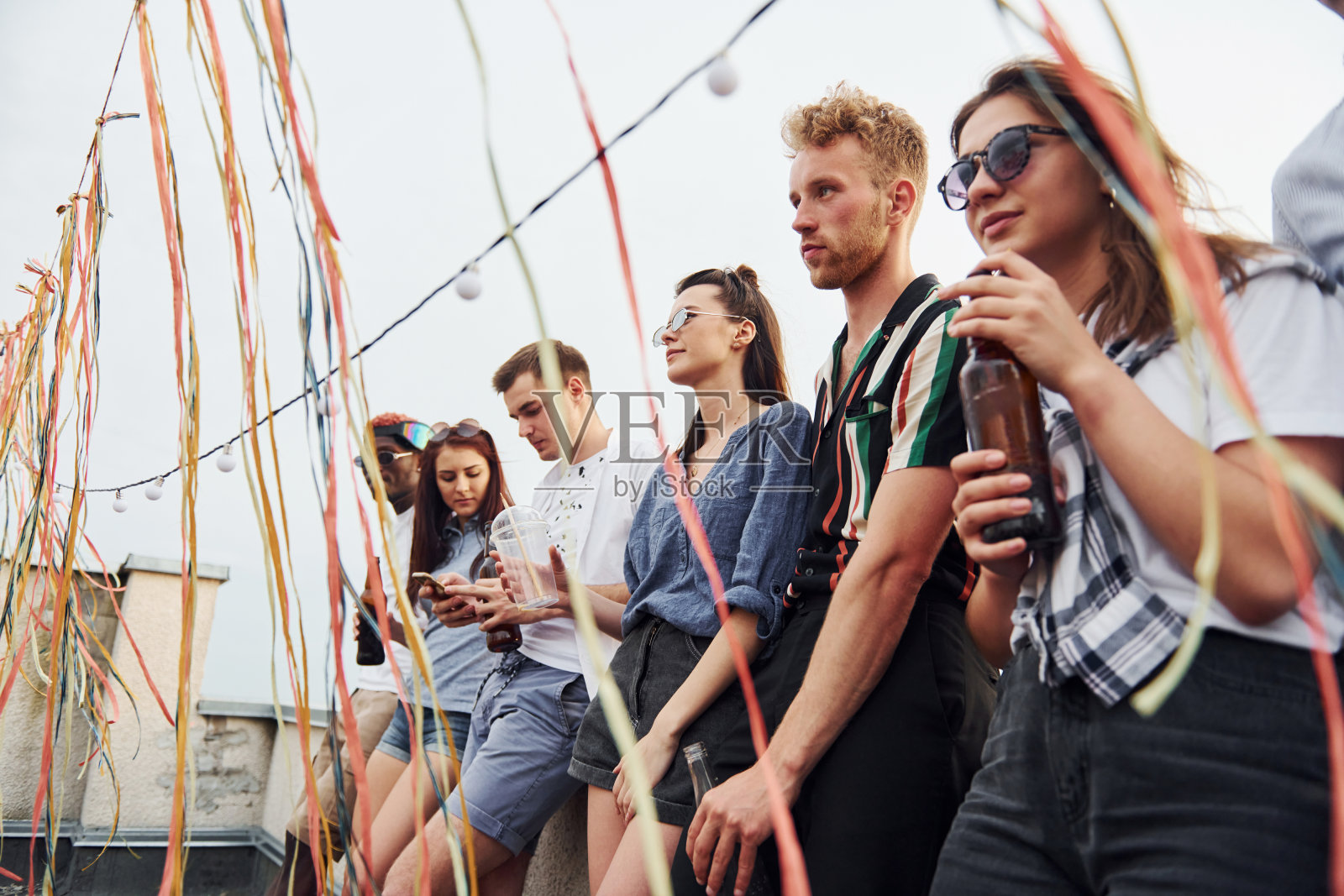靠在屋顶边缘的装饰。一群穿着便服的年轻人在白天聚会照片摄影图片