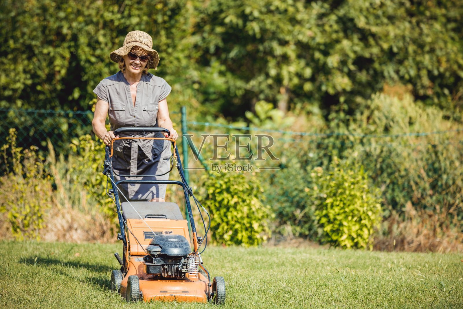 女人穿着雨靴用割草机在花园里割草,概念园艺工具照片摄影图片