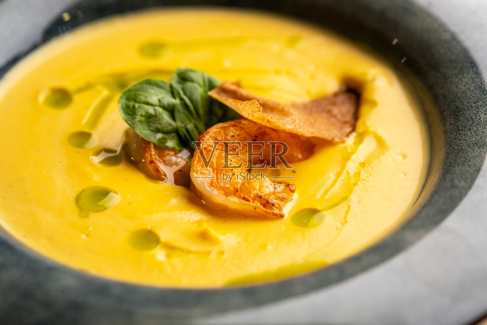 奶油南瓜汤配烤虾。汤在一个蓝色的盘子在黑色的背景。照片摄影图片