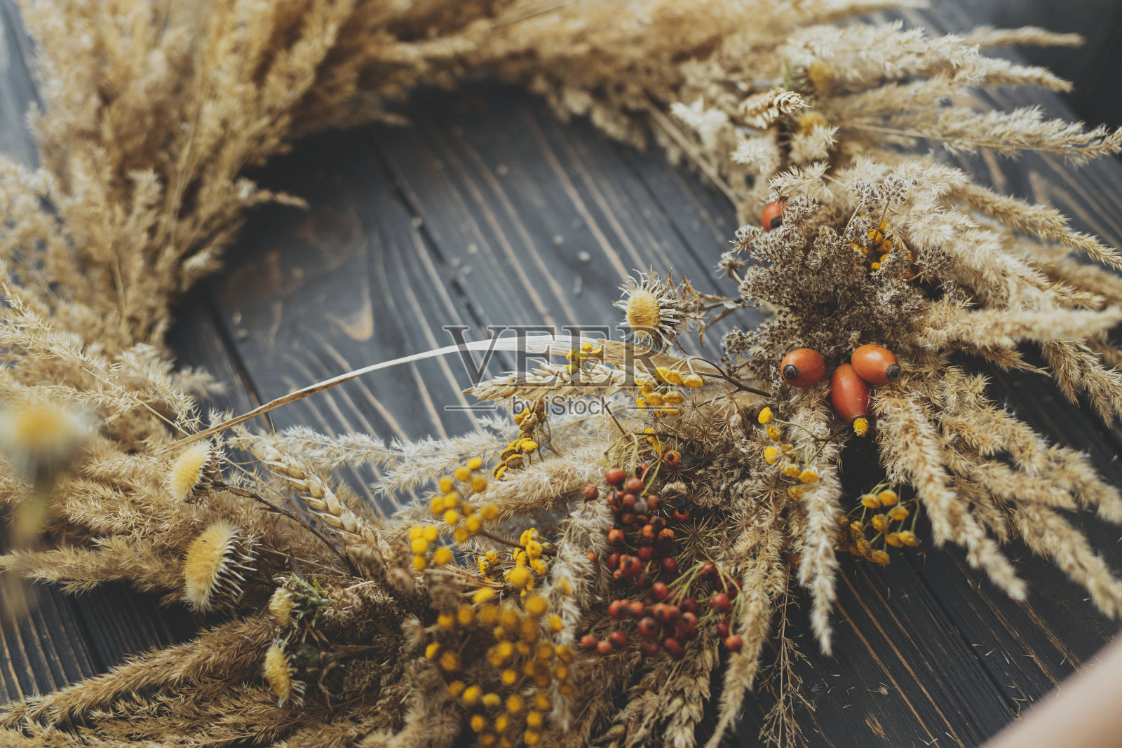 时尚的秋天乡村花环闭合。创意的波西米亚花环,干燥的潘巴斯草,唐茜野花,小麦,狗玫瑰浆果放在深色的木桌上。假日车间。细节照片摄影图片